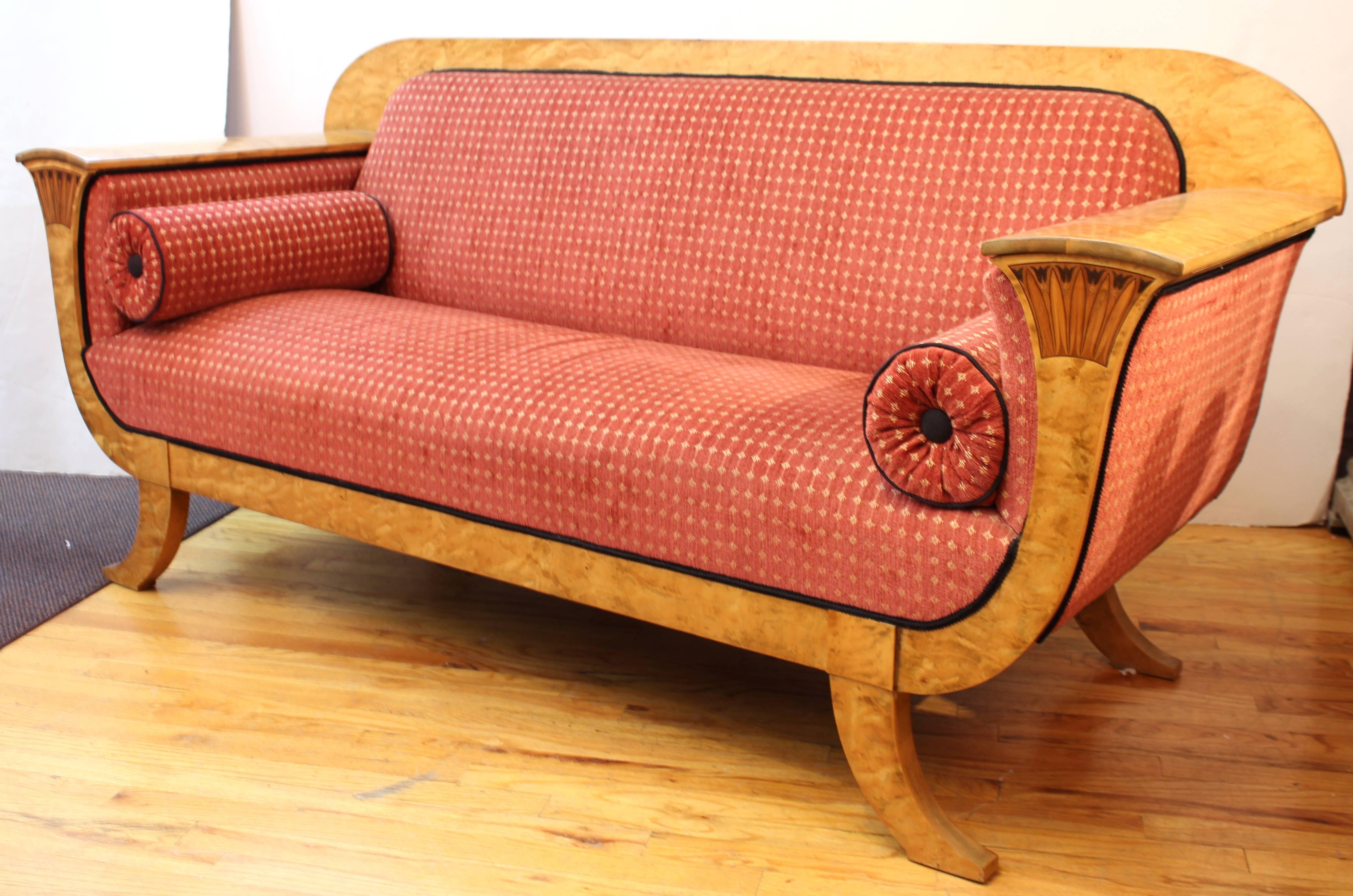 A Biedermeier sofa with a birch frame and luxurious red upholstery and cushions. The piece has low relief neoclassical accents near the armrests on the front. In good vintage condition having wear consistent with age and use.