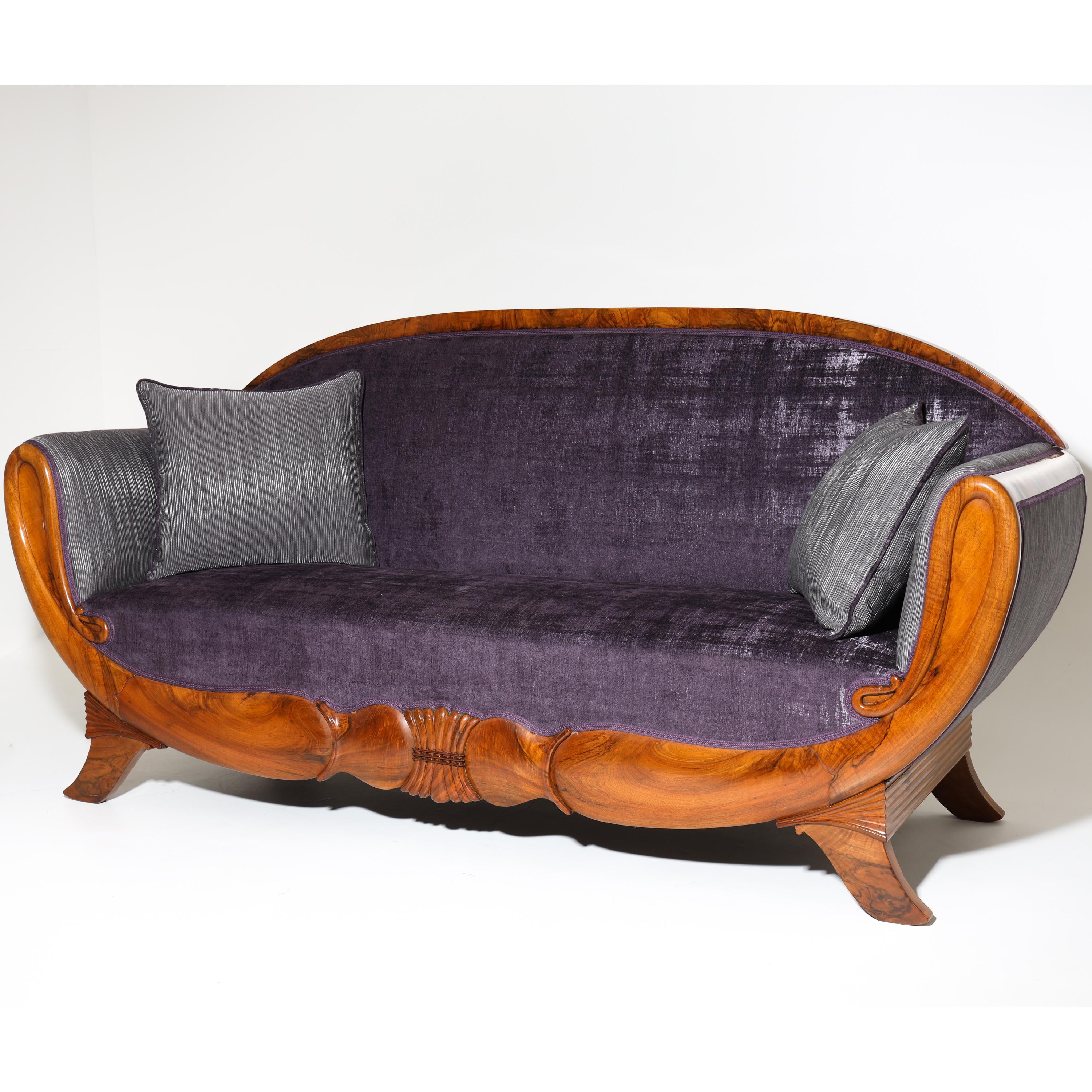 Biedermeier sofa in the style of Klussmann, in walnut, standing on flared legs with an arched carved frame and rounded backrest. The backrest and seat are covered with a high-quality violet fabric, the armrests are covered with a striped fabric on