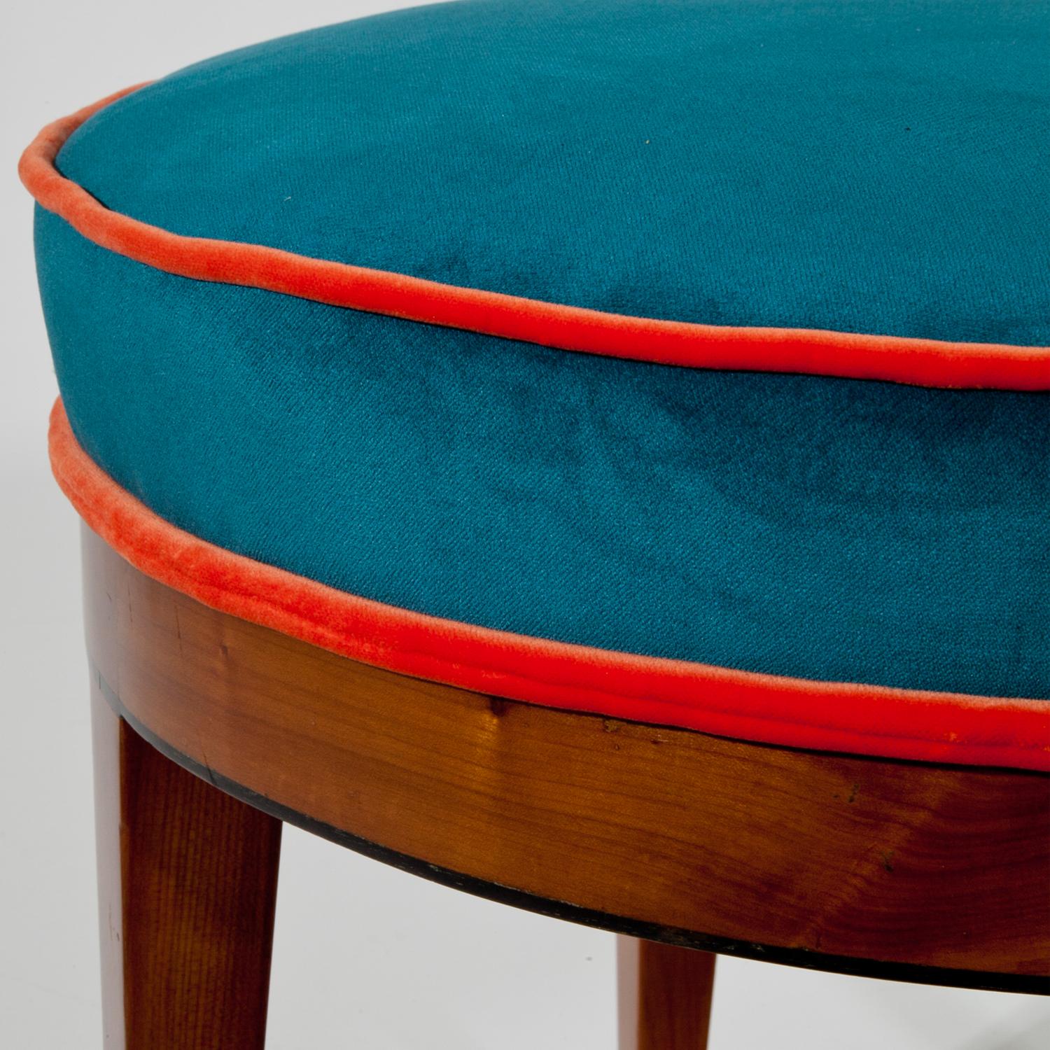 Round Biedermeier stool standing on tapered legs, made out of cherrywood. The railing is accentuated towards the lower edge in black. The stool was reupholstered with a blue fabric and orange piping.