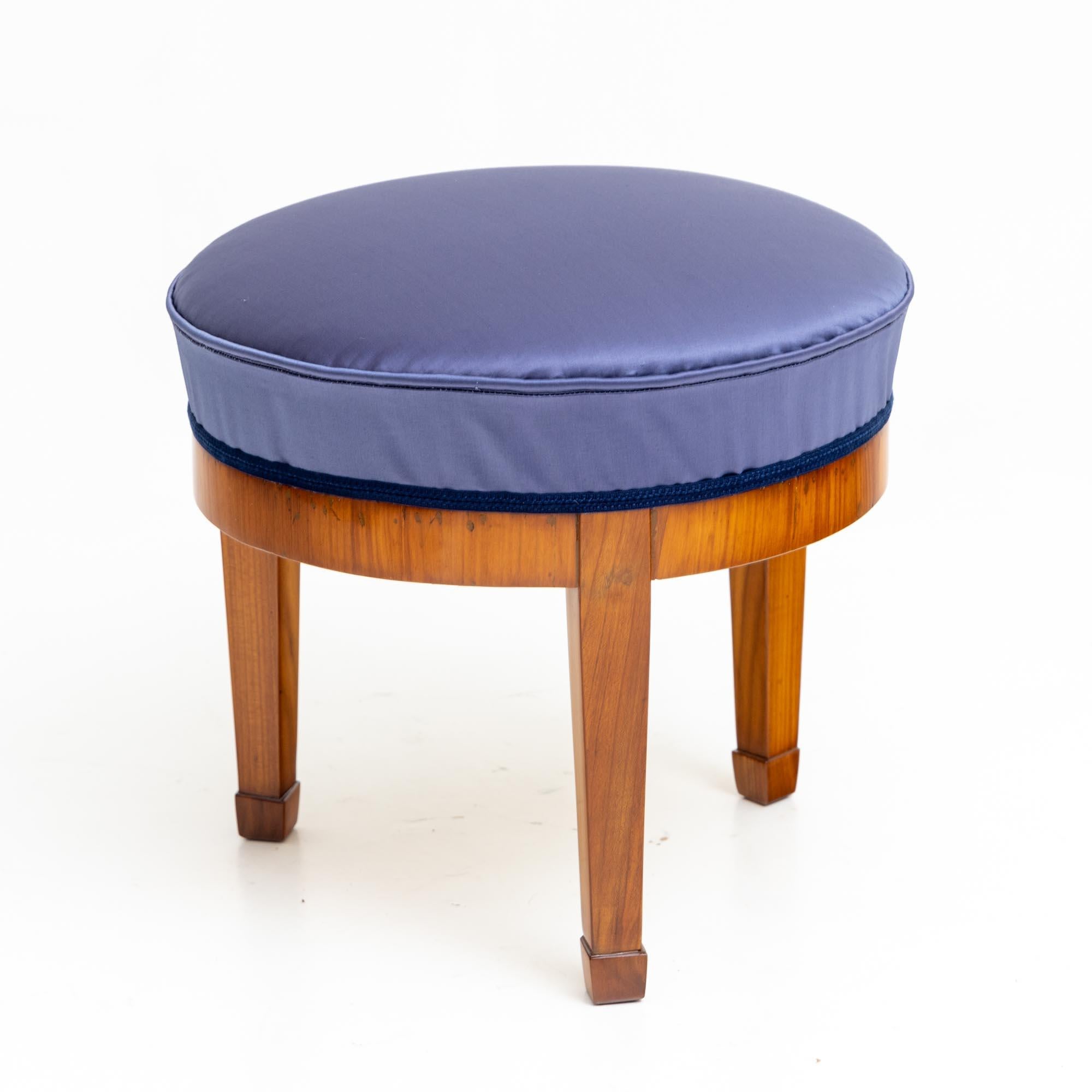 Small Biedermeier stool with three socketed and pointed legs and straight frame. The frame is veneered in cherry and polished by hand. The stool has been newly upholstered with a blue satin fabric.