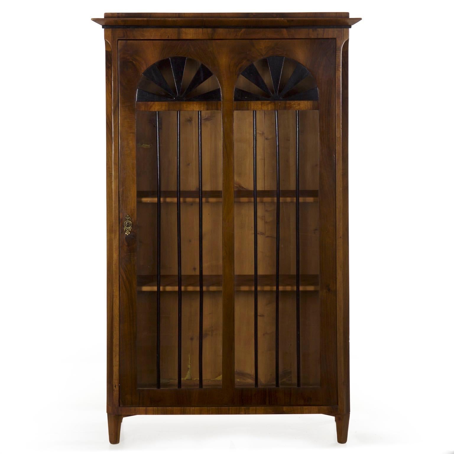 A rather unusual vitrine designed in the Biedermeier taste, it was likely crafted during the last quarter of the 19th century but perhaps as late as the turn of the century. The match-booked walnut veneers are striking along the length of the sides