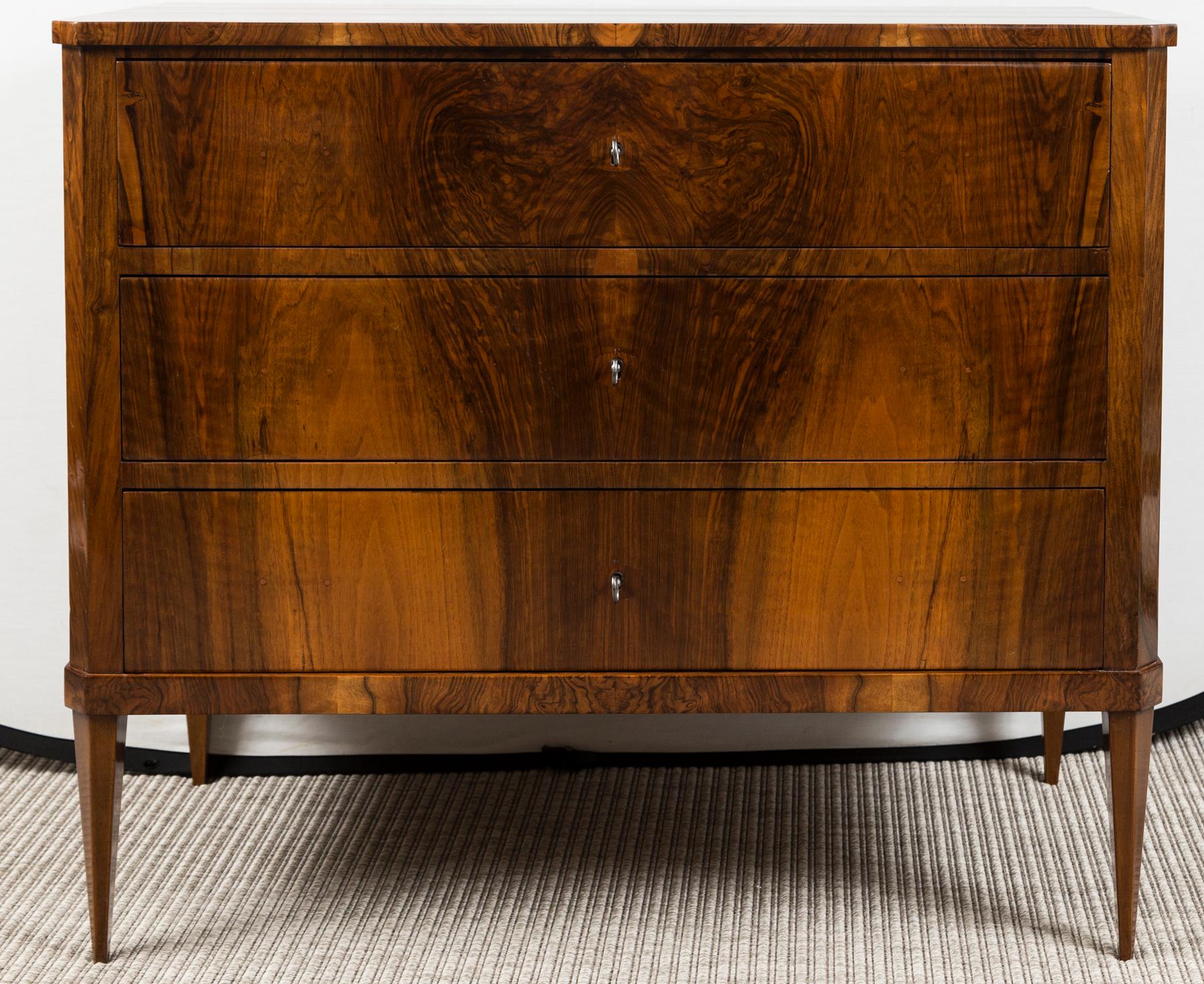 A stunning Biedermeier style walnut book matched veneer chest comprised of  three working drawers opening each with a key used as a pull and finishing on chamfered straight and tapered legs.

Origin: Germany

Condition: Excellent, entirely