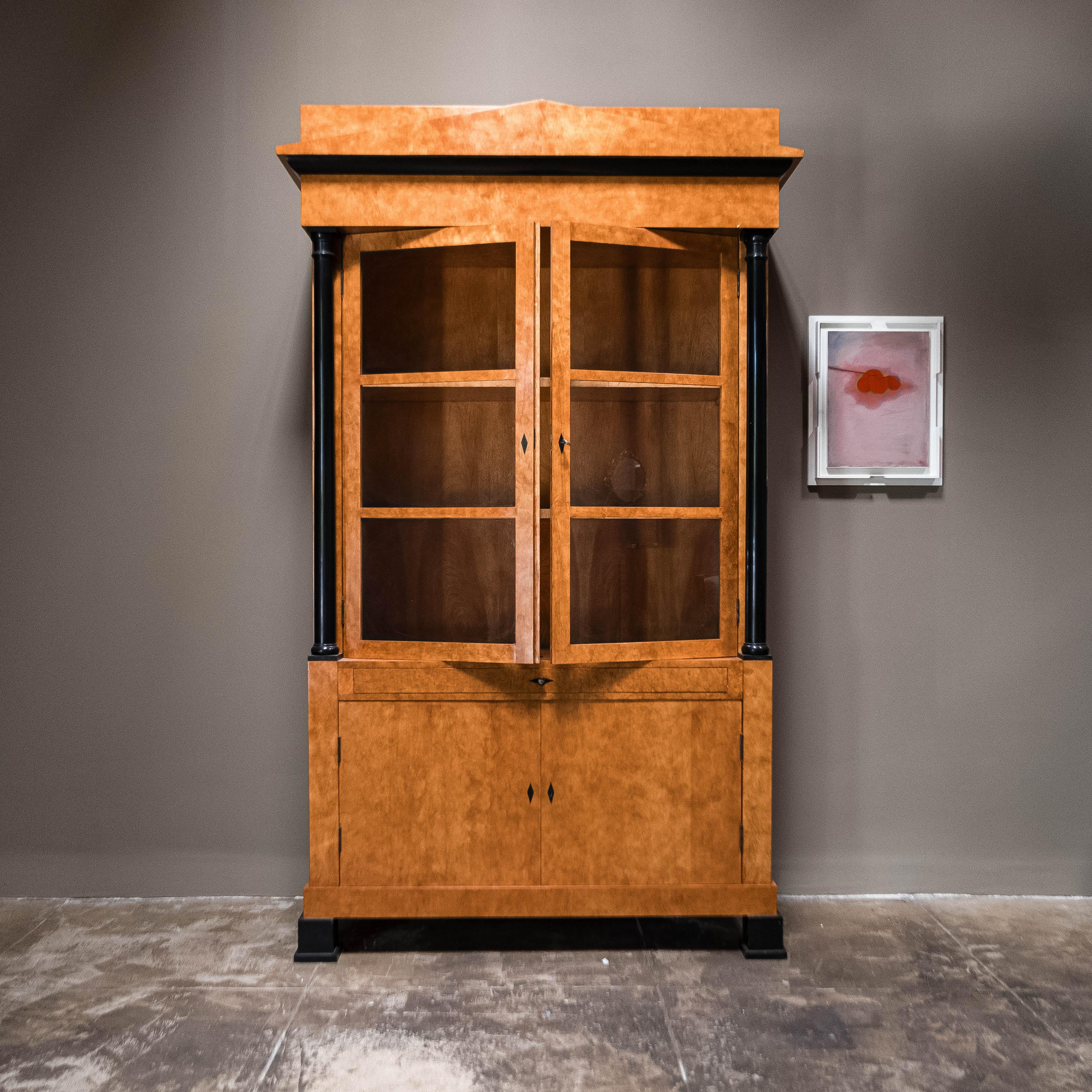 Splendida vetrina in legno da frutto in stile Biedermeier del XIX secolo. Questo squisito pezzo sfoggia un classico stile Biedermeier, realizzato con un ricco legno di frutta. Il piano d'ingresso è caratterizzato da un elegante architrave