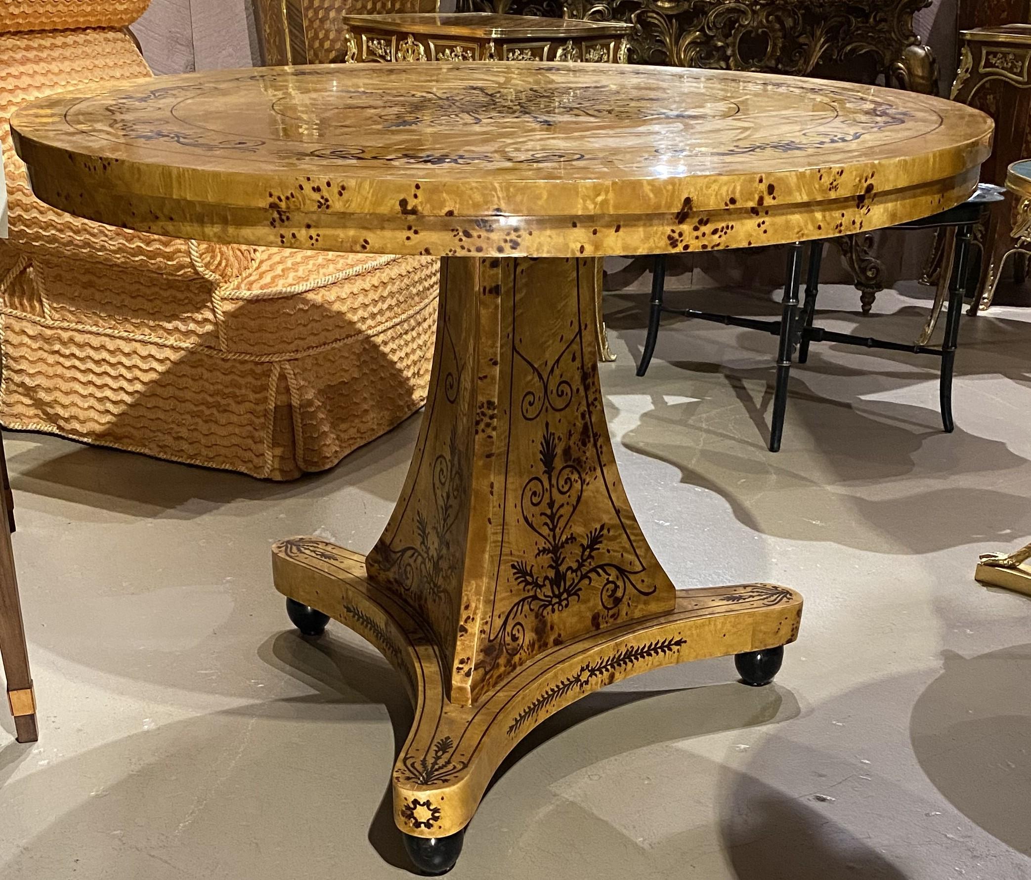 Magnifique table centrale ronde en bois de bourgogne de style Biedermeier, avec marqueterie décorative contrastée sur le plateau et le piédestal triangulaire avec base tripode et pieds en chignon. Datant du XXe siècle, en très bon état, avec de
