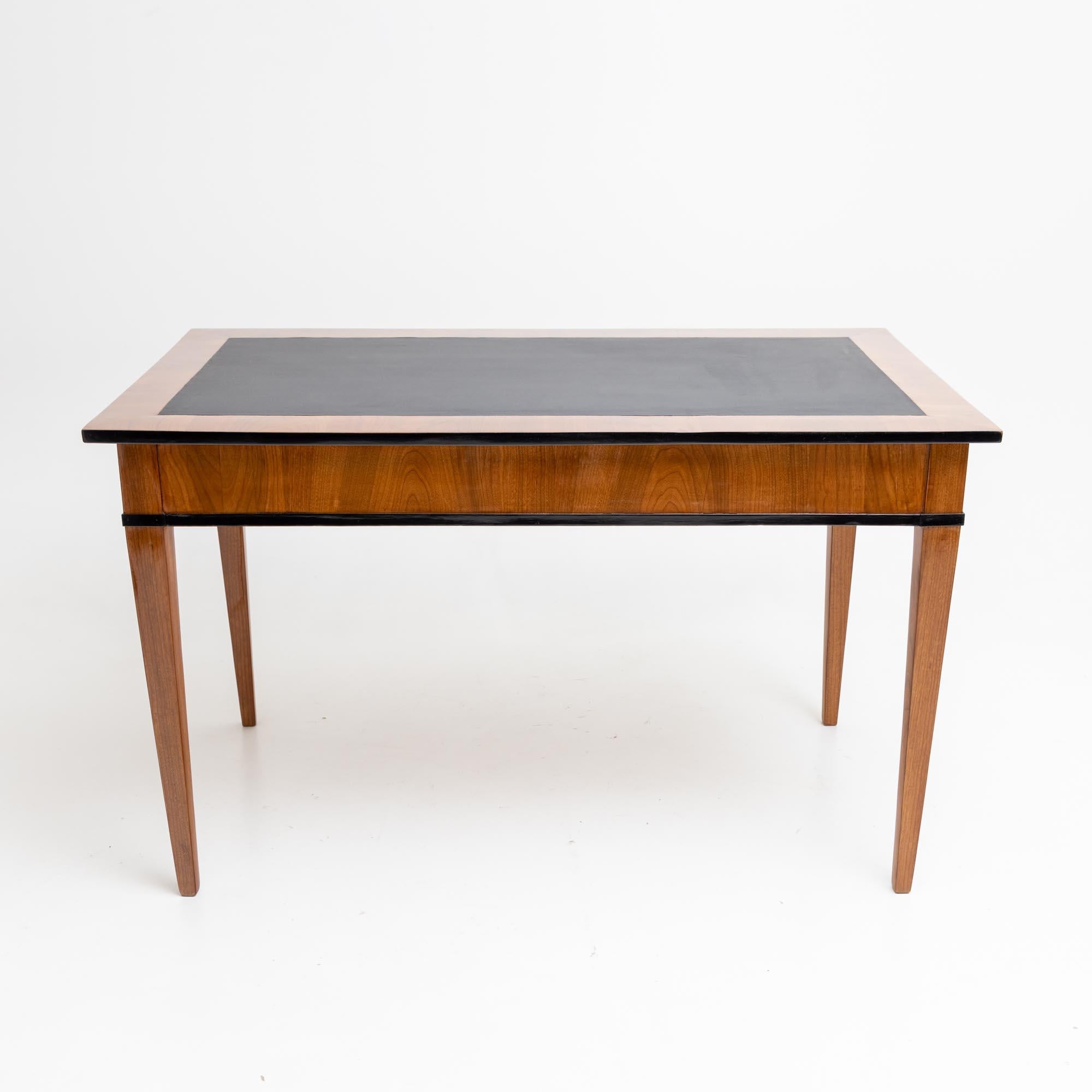 Desk in cherry veneer on high square legs with straight frame and two drawers. The edges are ebonised, the writing surface is covered with black imitation leather. Restored and hand-polished condition.