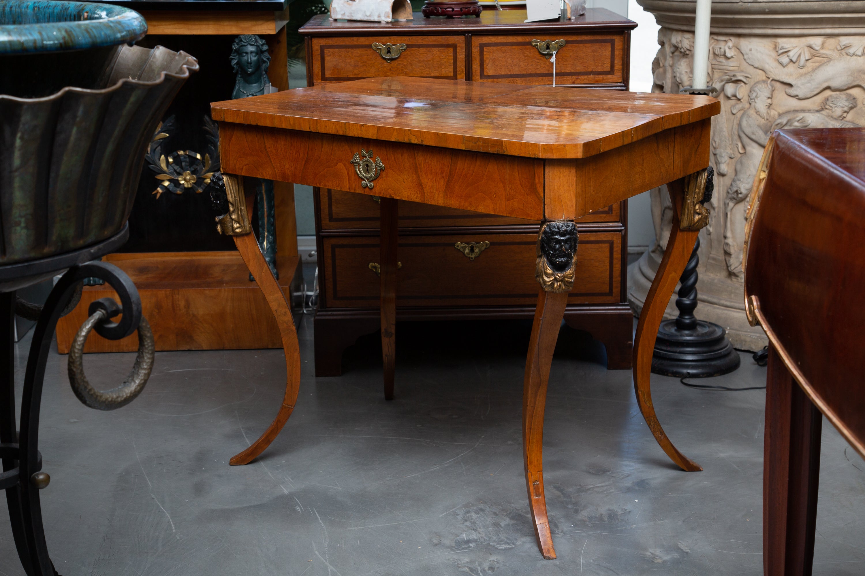 This is a refined Biedermeier walnut ebonized and parcel gilt side table, the top with straight edge over a long frieze drawer and supported by graceful out-curved legs with ebonized and parcel gilt masks on the knees, 19th Century.