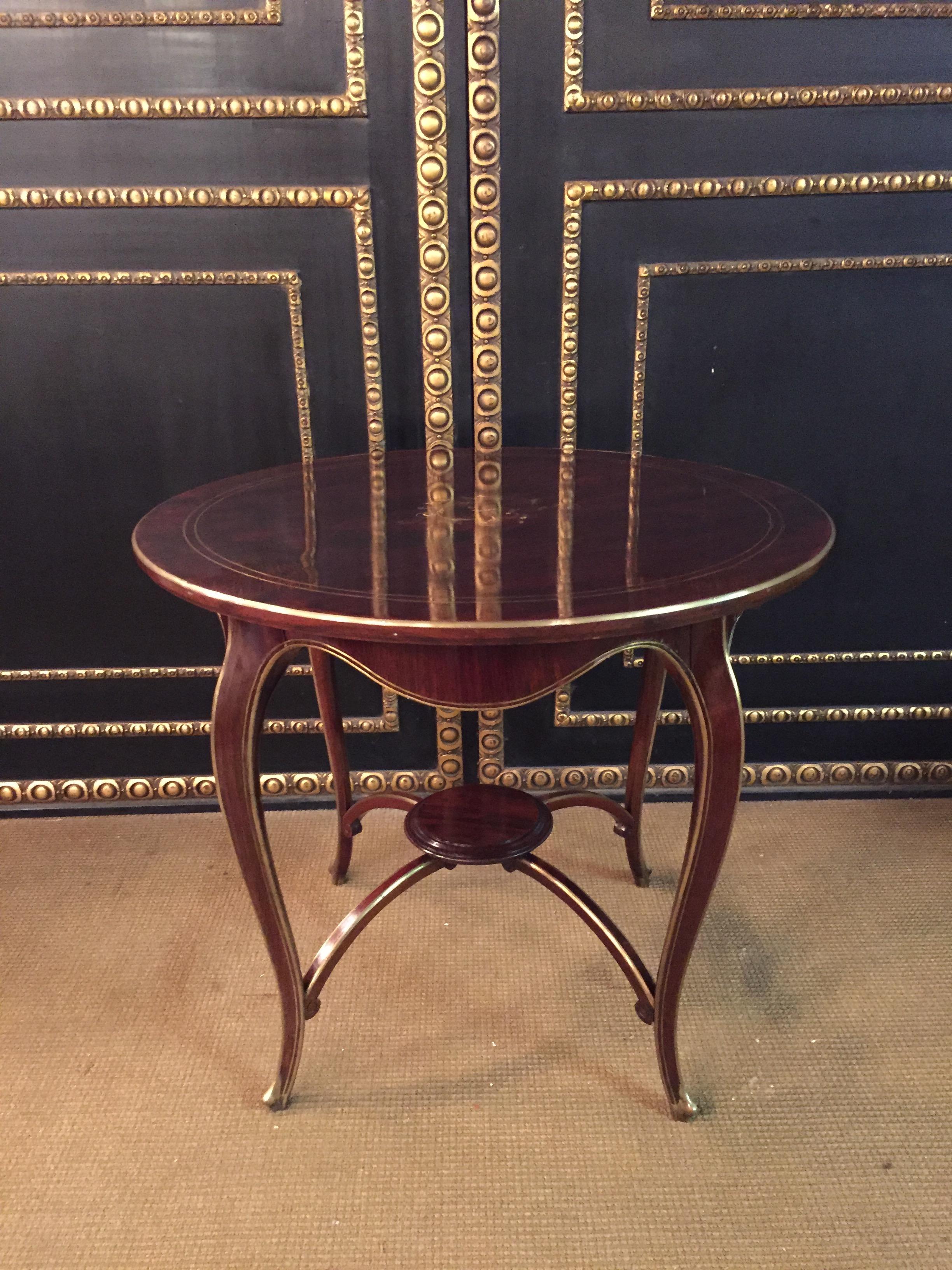 Solid wood a, partly blackened. Slightly protruding round cover plate on curved legs with fine brass framing connected by an intermediate plate.
The plate has fine inlays inserted above.