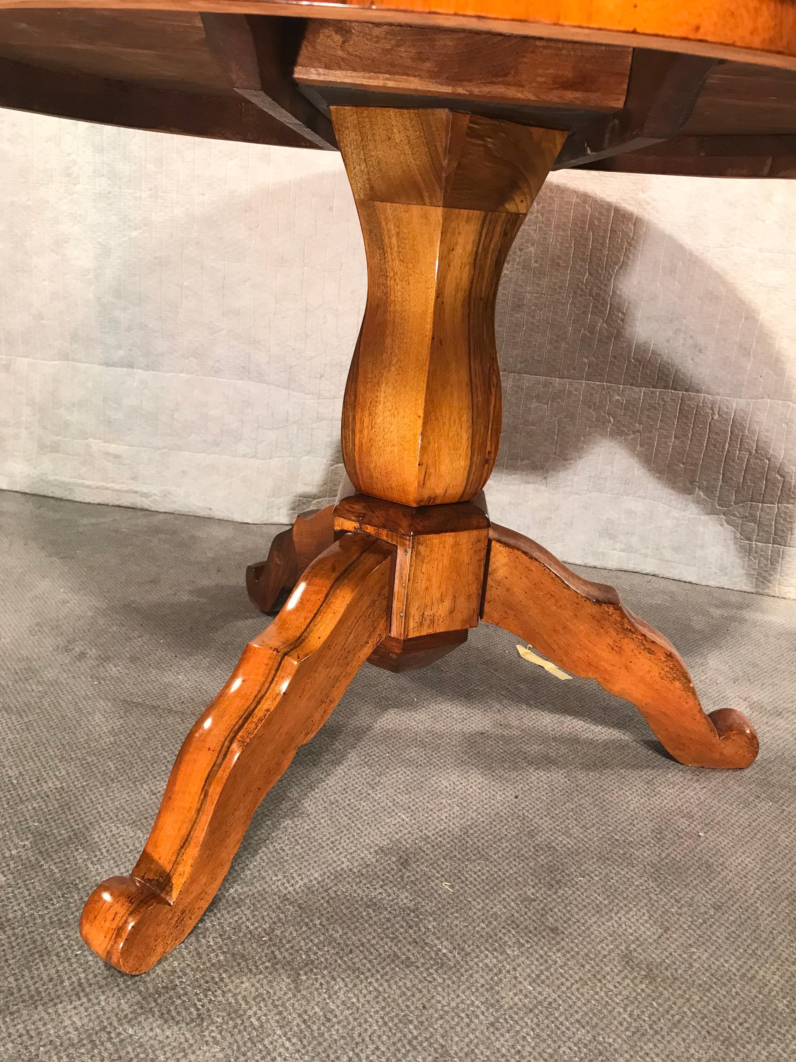 Dieser einzigartige Biedermeier-Tisch ist wirklich ein Meisterwerk. Seine Besonderheit ist die schöne Maserung des Nussbaumfurniers auf der Platte, die elegant von einem Dreibeinfuß und einer zentralen Säule getragen wird. Die Handwerkskunst und die