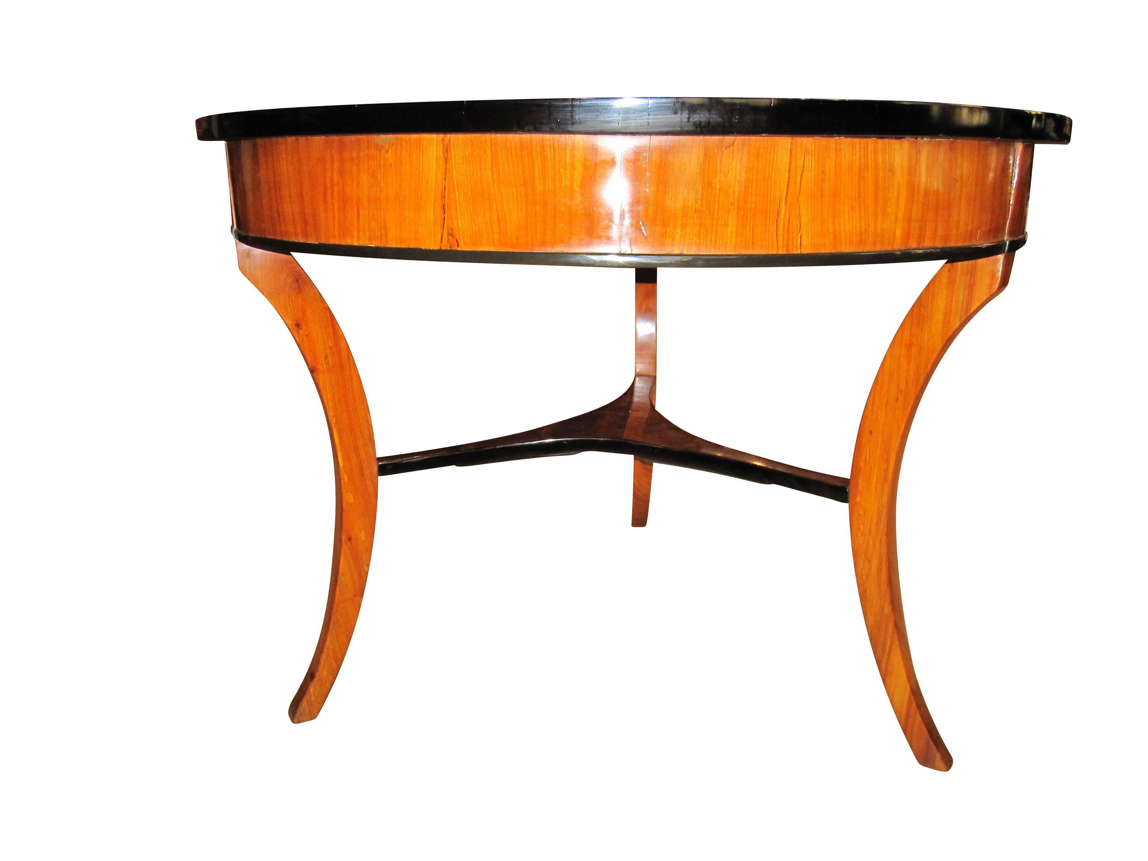 Elegant, round three-legged Biedermeier table. The plate is made with star-shaped cherry veneer. In the middle there is a circle made from elm-roots veneer and surrounded by a ebony inlay. Some parts like the tableau between the concave legs or the