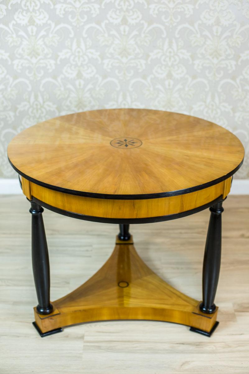 We present you a piece of furniture of a noble, simple form that is typical for the Biedermeier style; with a characteristic juxtaposition of light and black veneer.
The round table is supported on three turned legs in the shape of columns, which