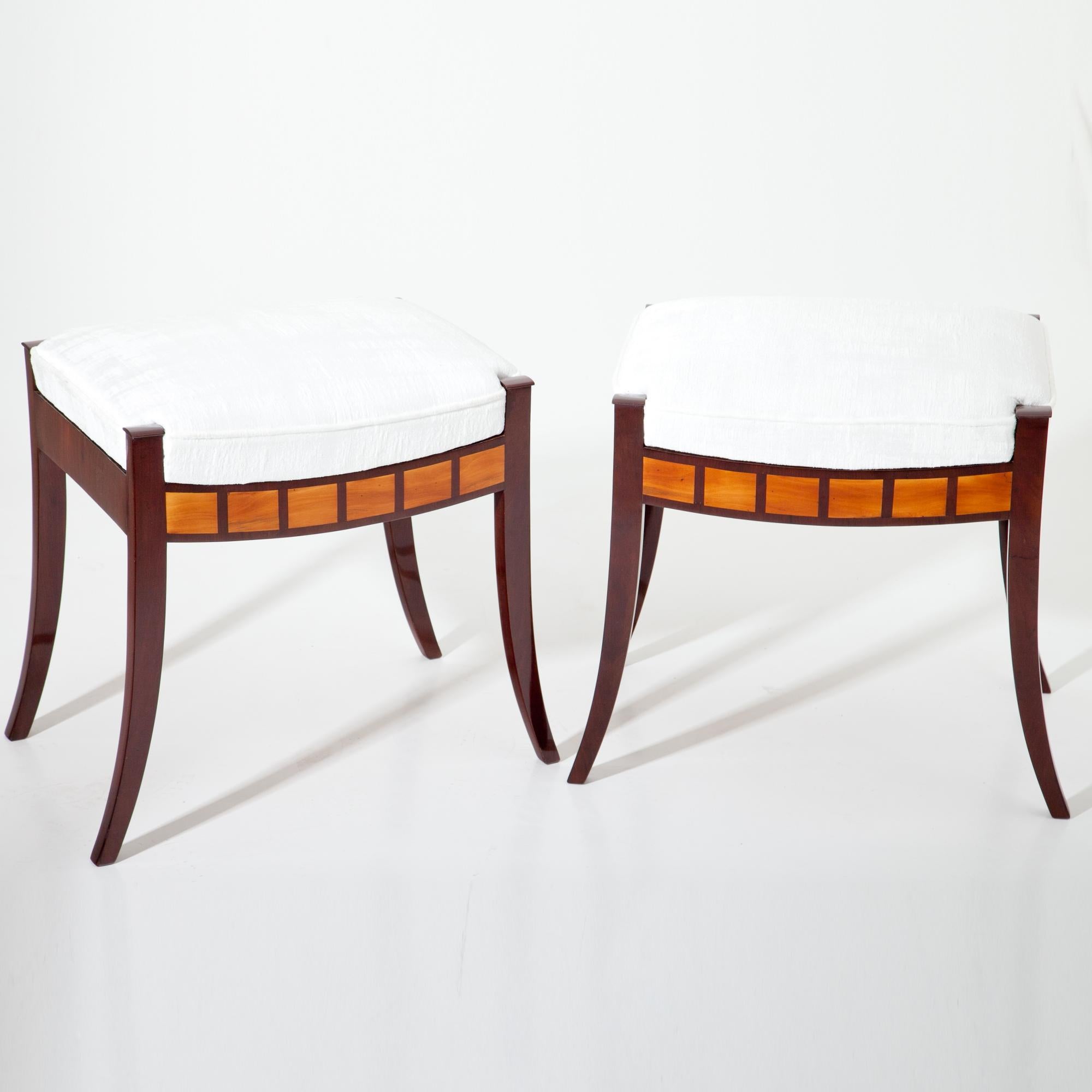 Pair of Biedermeier Tabourets, standing on tapered bent legs out of Mahogany with a rectangular seat. The front rails are decorated with rectangular fruitwood inlays. The seats were reupholstered with a white fabric.