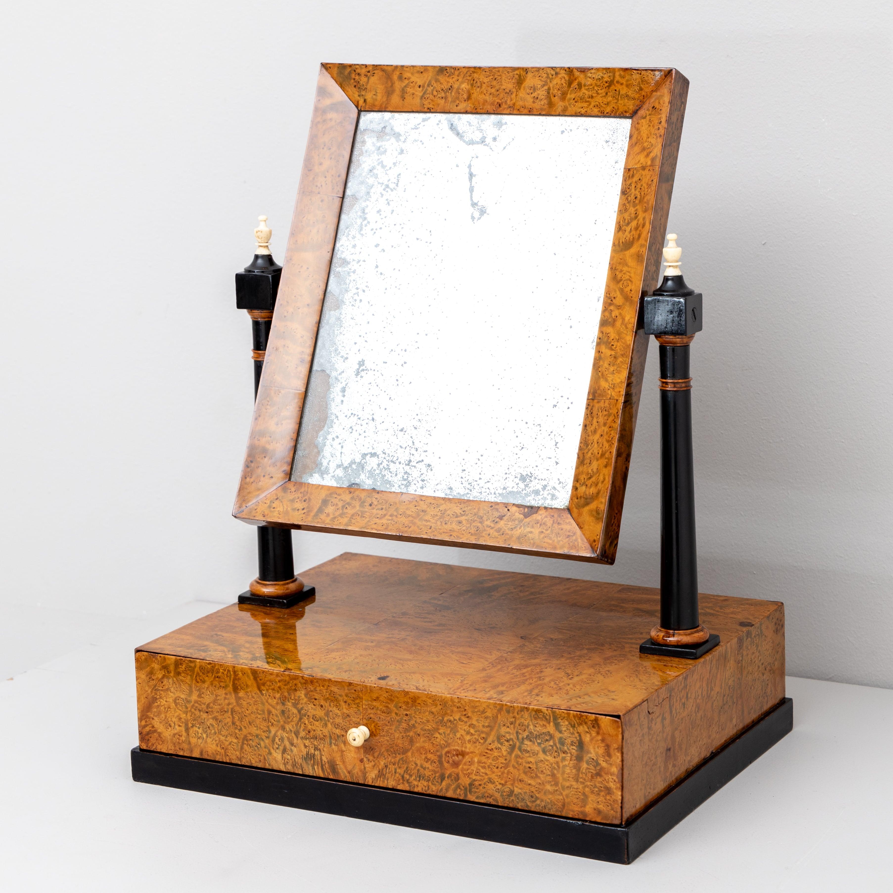Petit miroir de table plaqué en racine de thuya avec un tiroir et un miroir rectangulaire inclinable. Le miroir est soutenu par deux colonnes ébonisées. L'ancien miroir est aveugle par endroits.