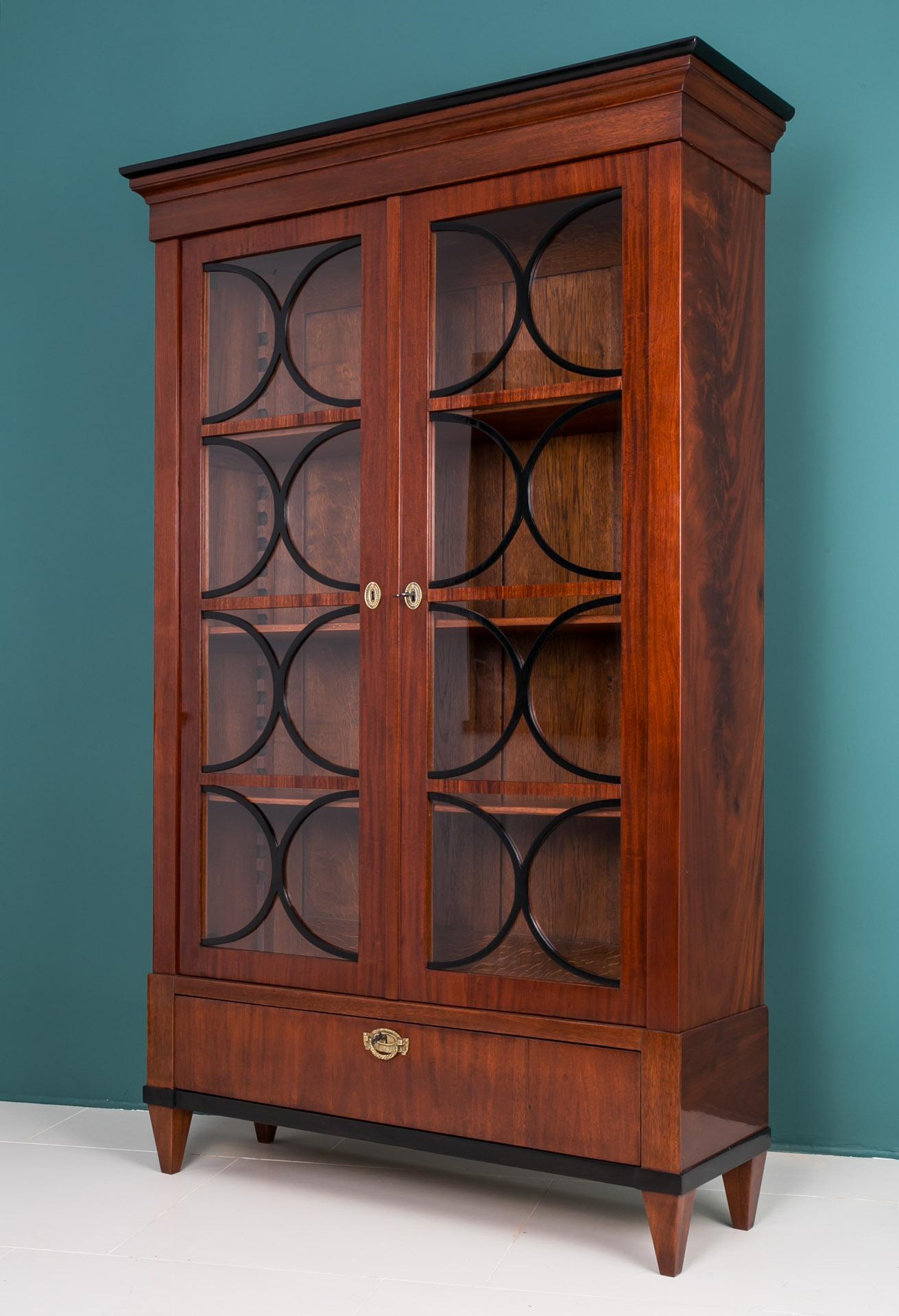 This Biedermeier vitrine comes from Austria and was made in 19th century. The piece is made of oak wood veneered with mahogany. The doors have got unique muntins emphasizing its style and elegance. It features 3 shelves with adjustable height system