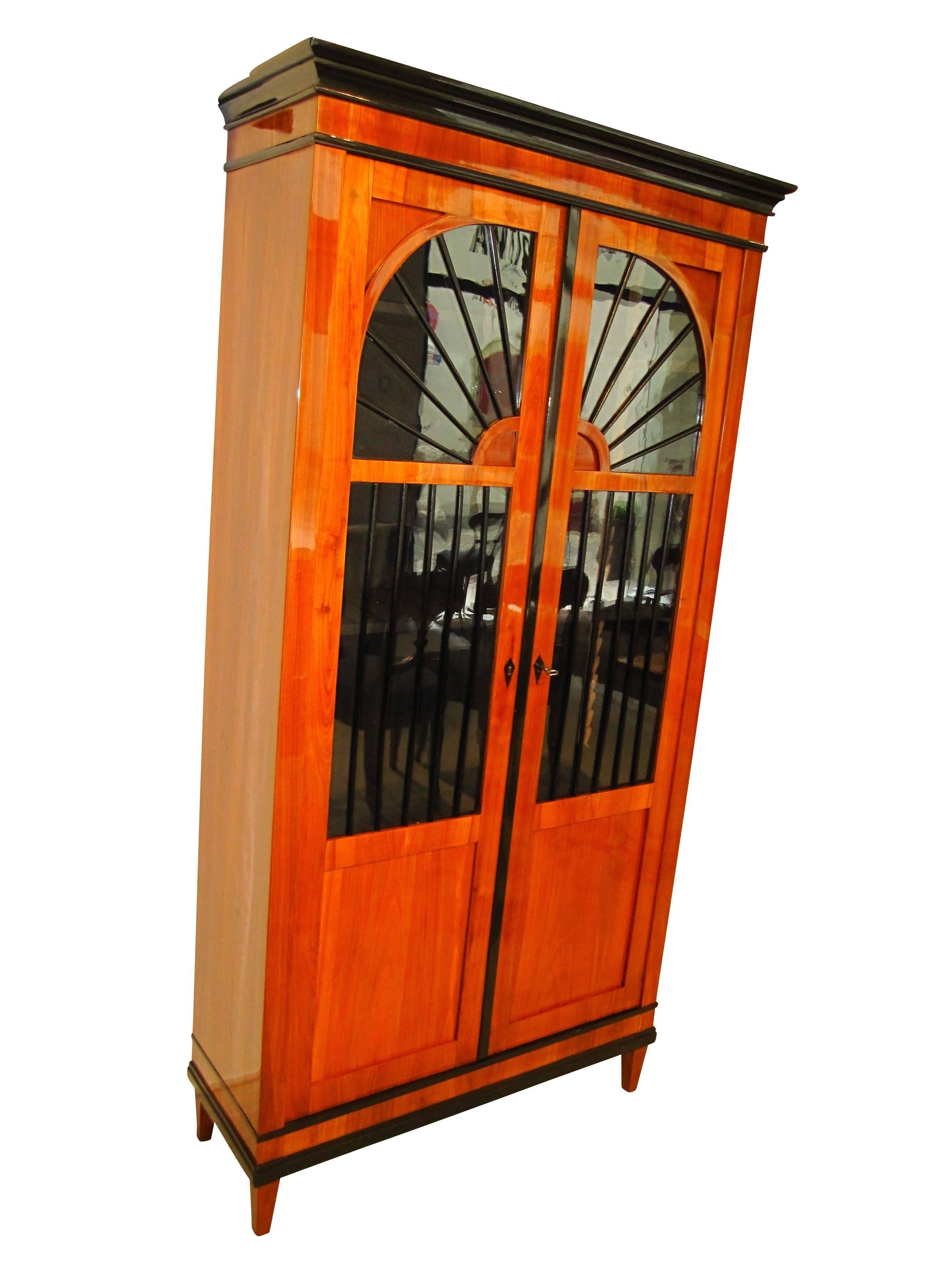 Wonderful and very elegant early Biedermeier vitrine, bookcase or display case.
It has a lovely cherry veneer and solid wood with ebonized glazing bars. The low width makes the furniture seem very light and not dominant in the room.

The bookcase