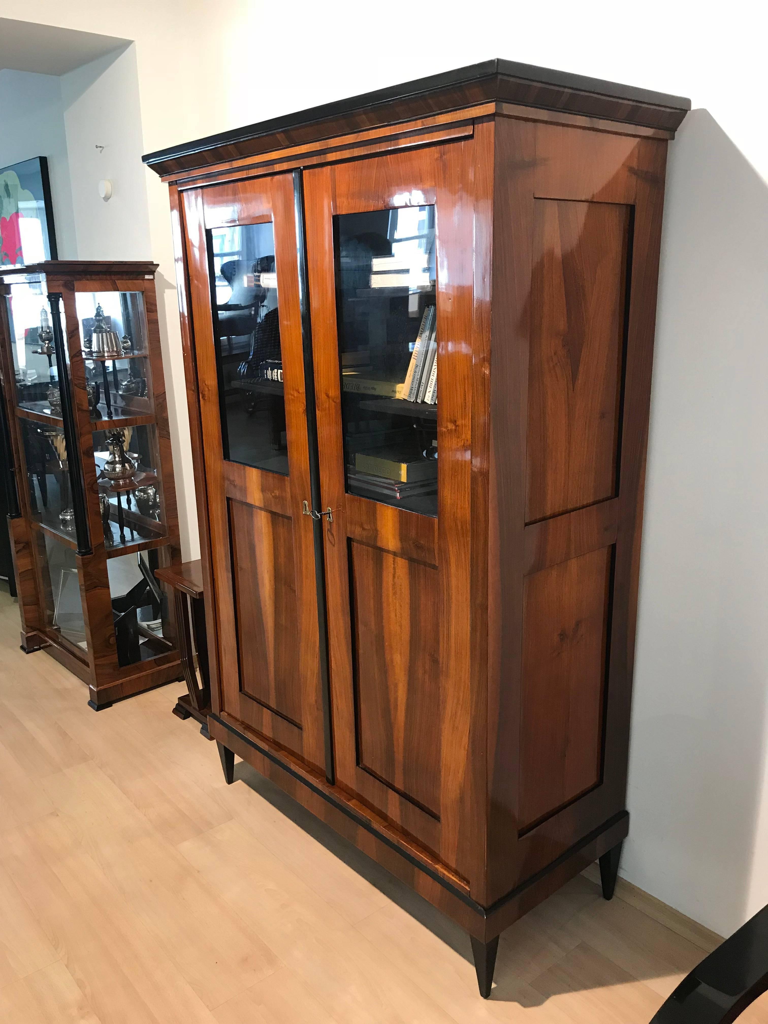 Beautiful classicist Biedermeier Vitrine / Showcase from Germany about 1825.

Wonderful book-matched Walnut Veneer and original brass fittings.

Two doors and with glasses in the upper half of the front door. 
On the inside it has 5 adjustable
