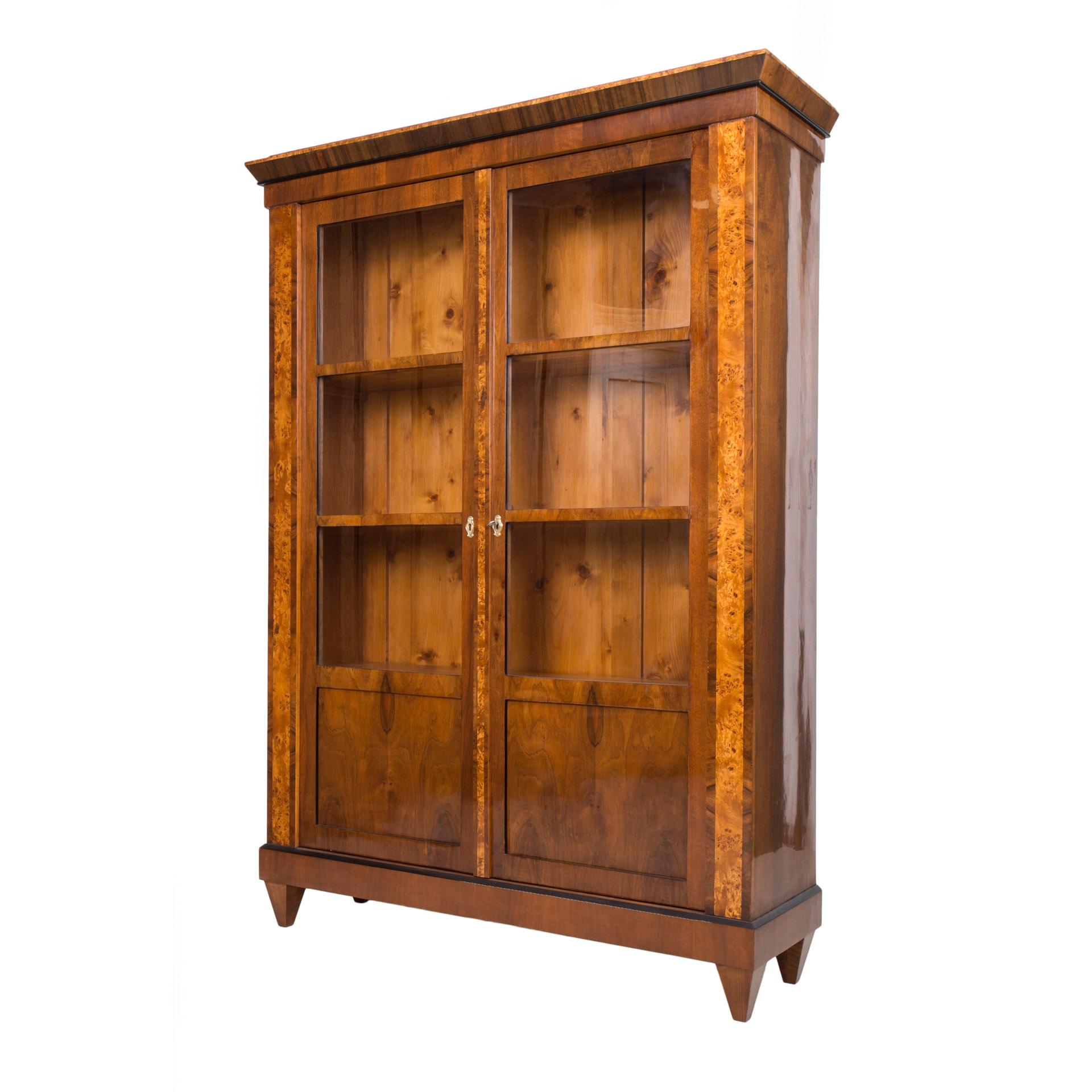 This Biedermeier vitrine comes from Germany and was made in 19th century. It is made of coniferous wood, veneered with walnut. It has undergone a professional renovation process. The surface is finished with shellac polish, applied by hand, which