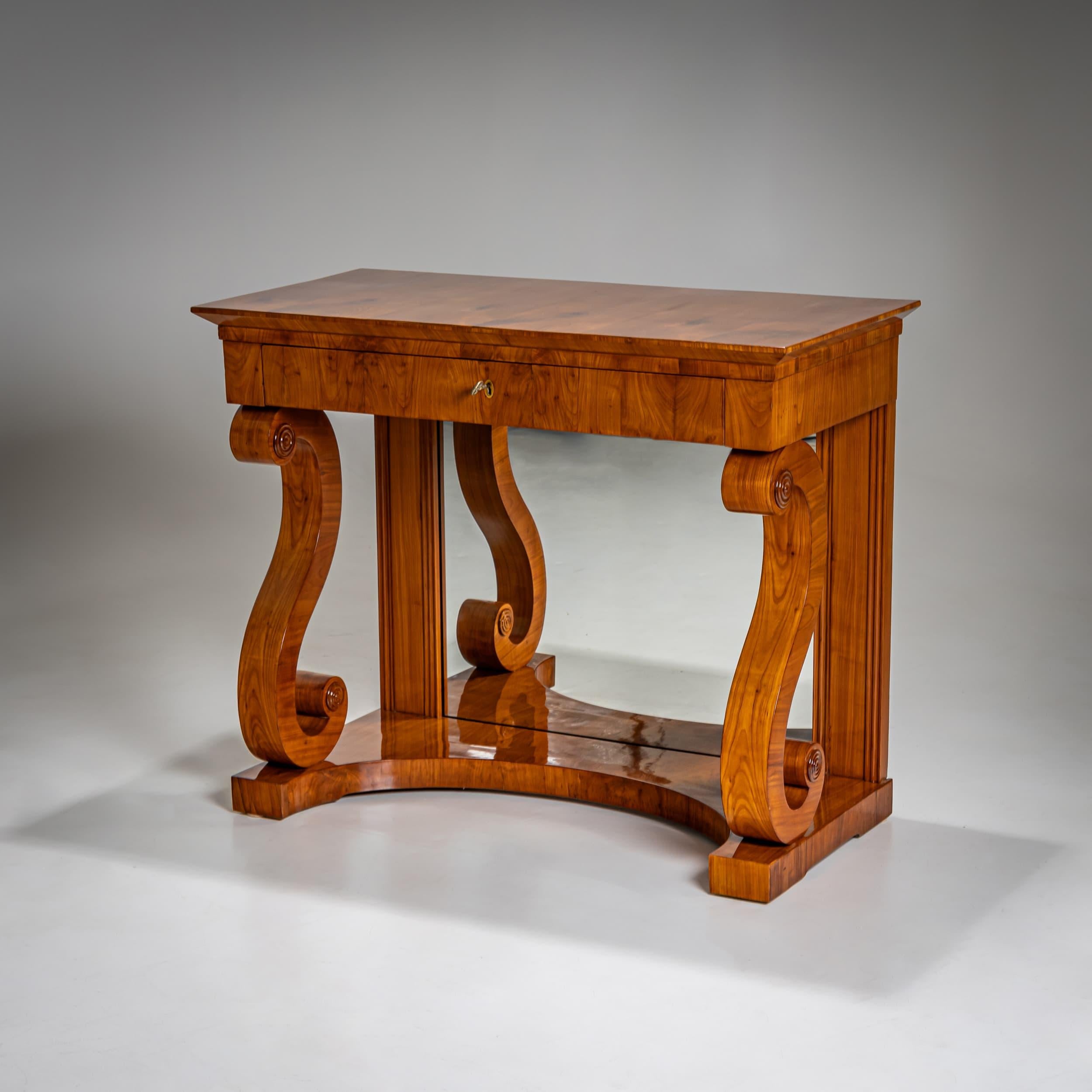 Elegante console da parete Biedermeier in legno di ciliegio, con un cassetto e un pannello posteriore a specchio. Le gambe anteriori sono disegnate come doppie volute stilizzate, mentre la base è concava. La console è rivestita in ciliegio ed è