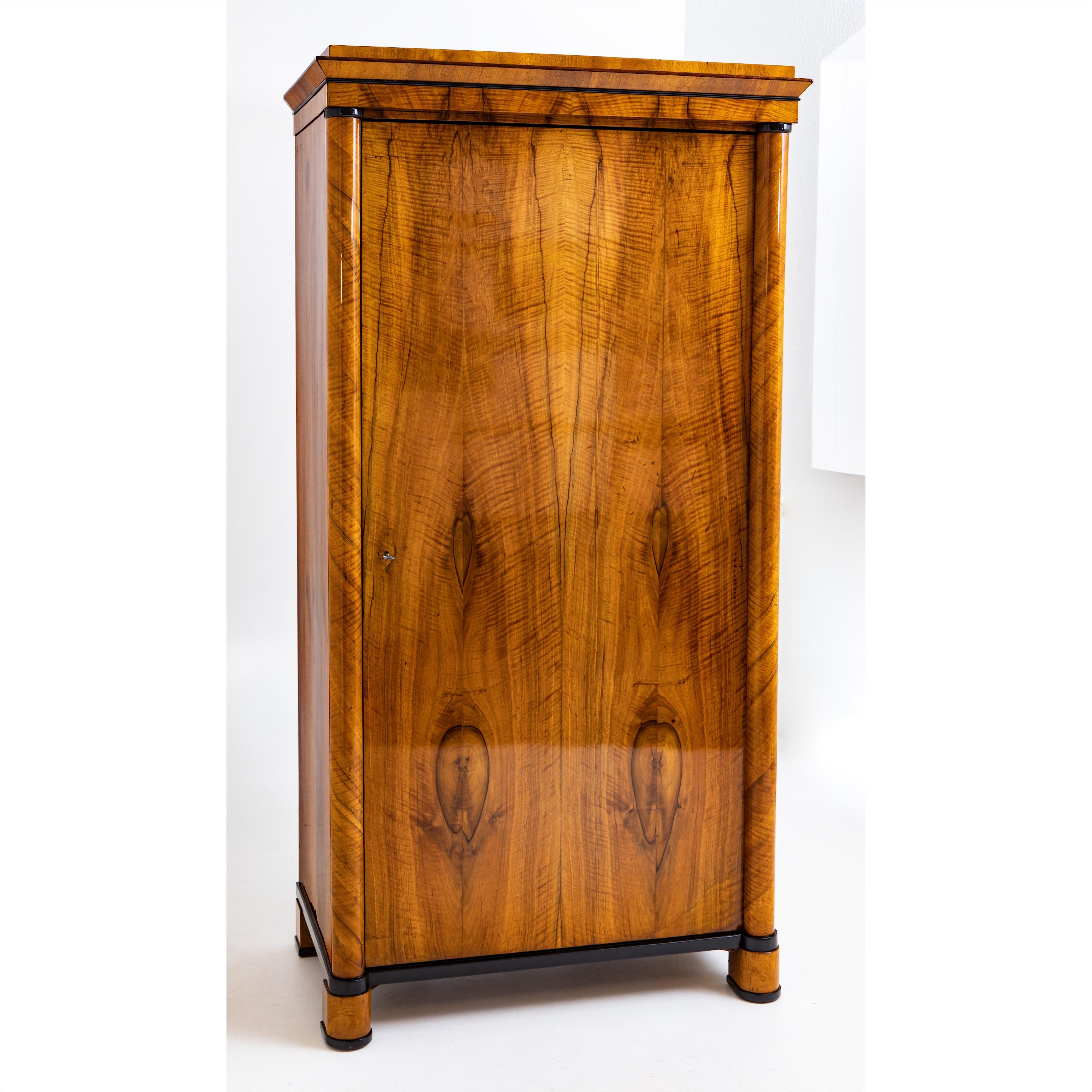 Single door Biedermeier cabinet with ebonized details and rounded corners. Very nice veneer pattern. The straight cornice is profiled and optically structured by ebonized strips. The interior division consists of five height-adjustable shelves. The
