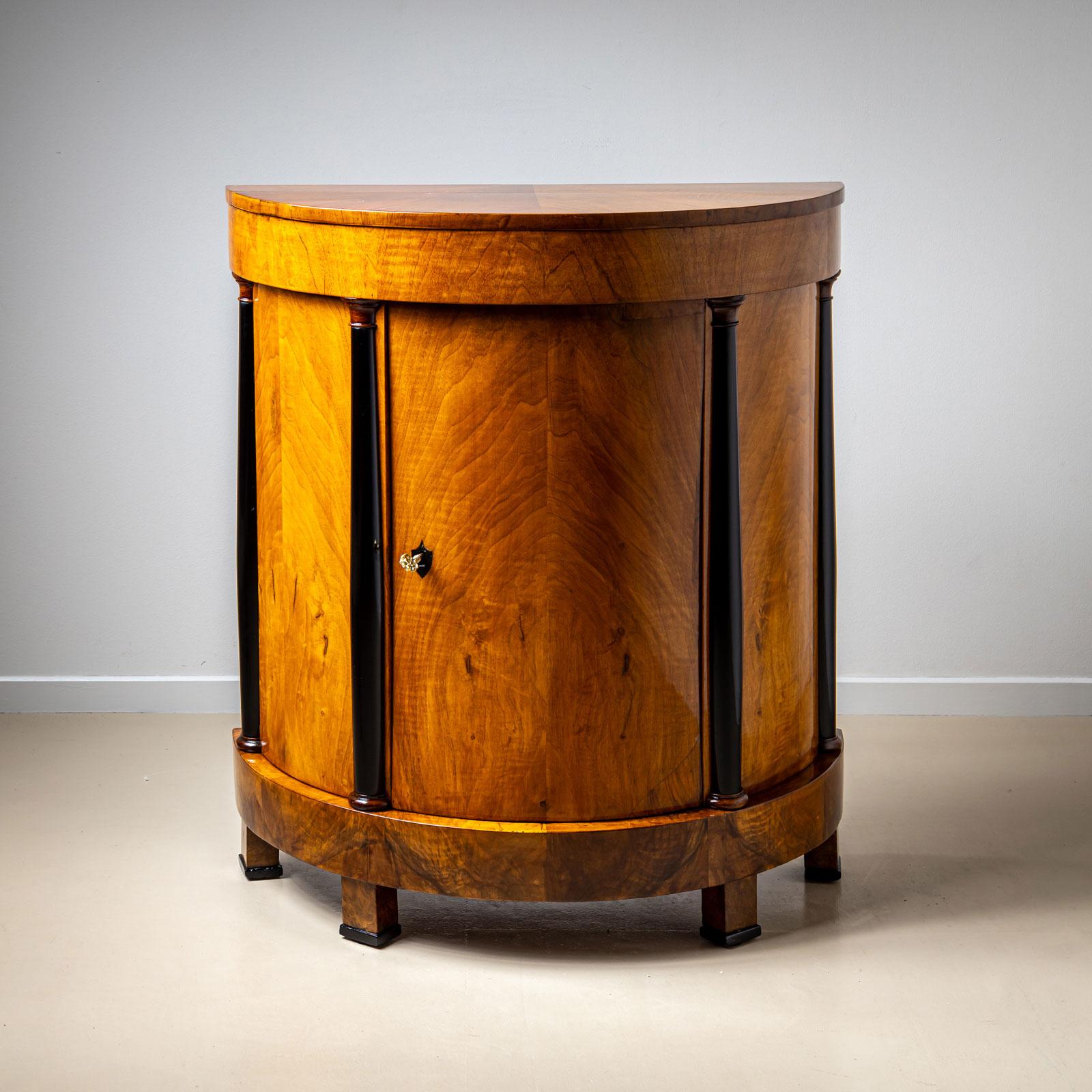 Demi-cabinet Biedermeier démilune de belle facture provenant d'Allemagne, vers 1820. Cette élégante pièce comporte une porte verrouillable avec des moulures en demi-colonne, magnifiquement plaquée en noyer avec des accents ébonisés. L'intérieur