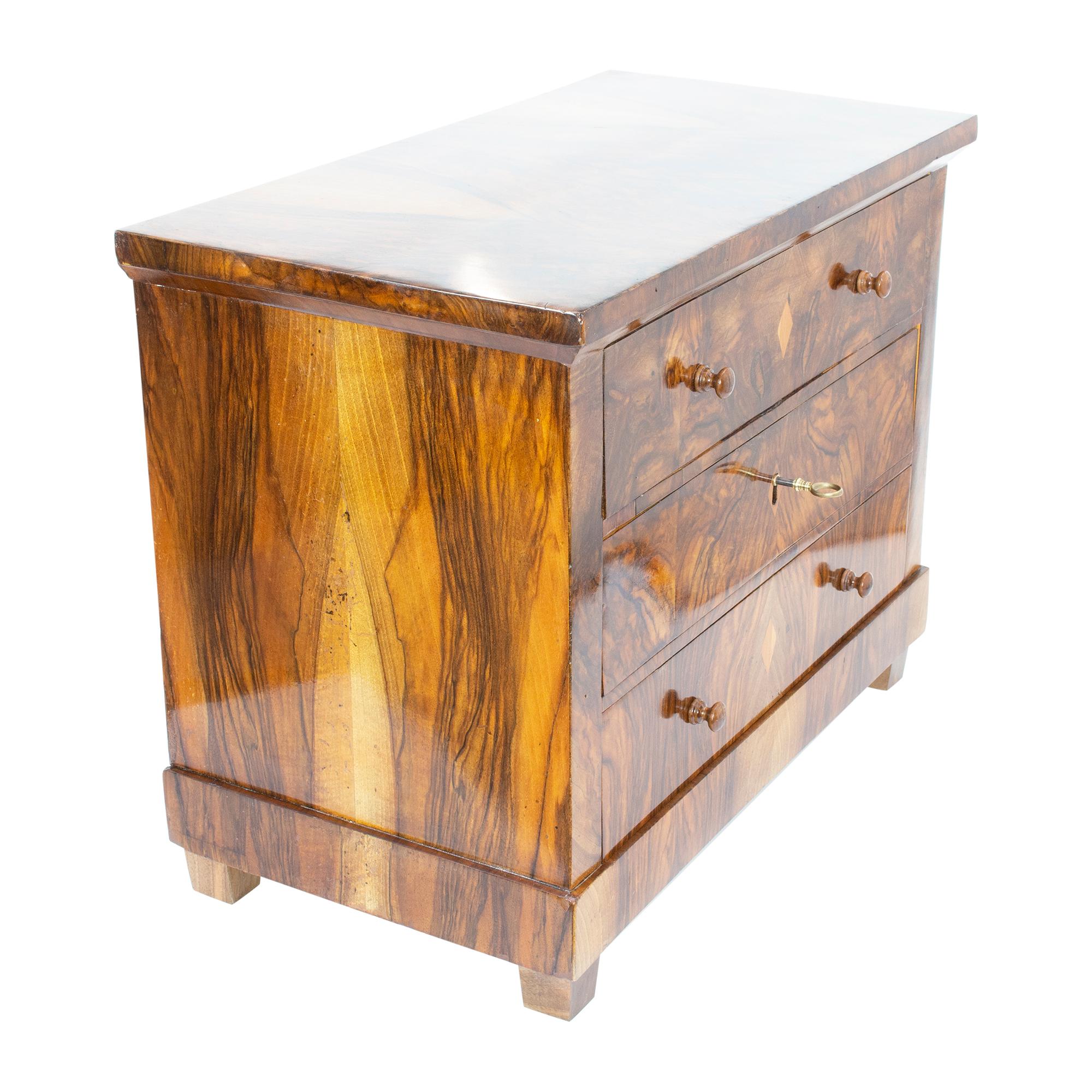 The miniature or model chest of drawers dates back to the Biedermeier period and was made with walnut veneer on a softwood body. The chest of drawers is in very good restored condition. The middle drawer is lockable. The feet of the chest of drawers