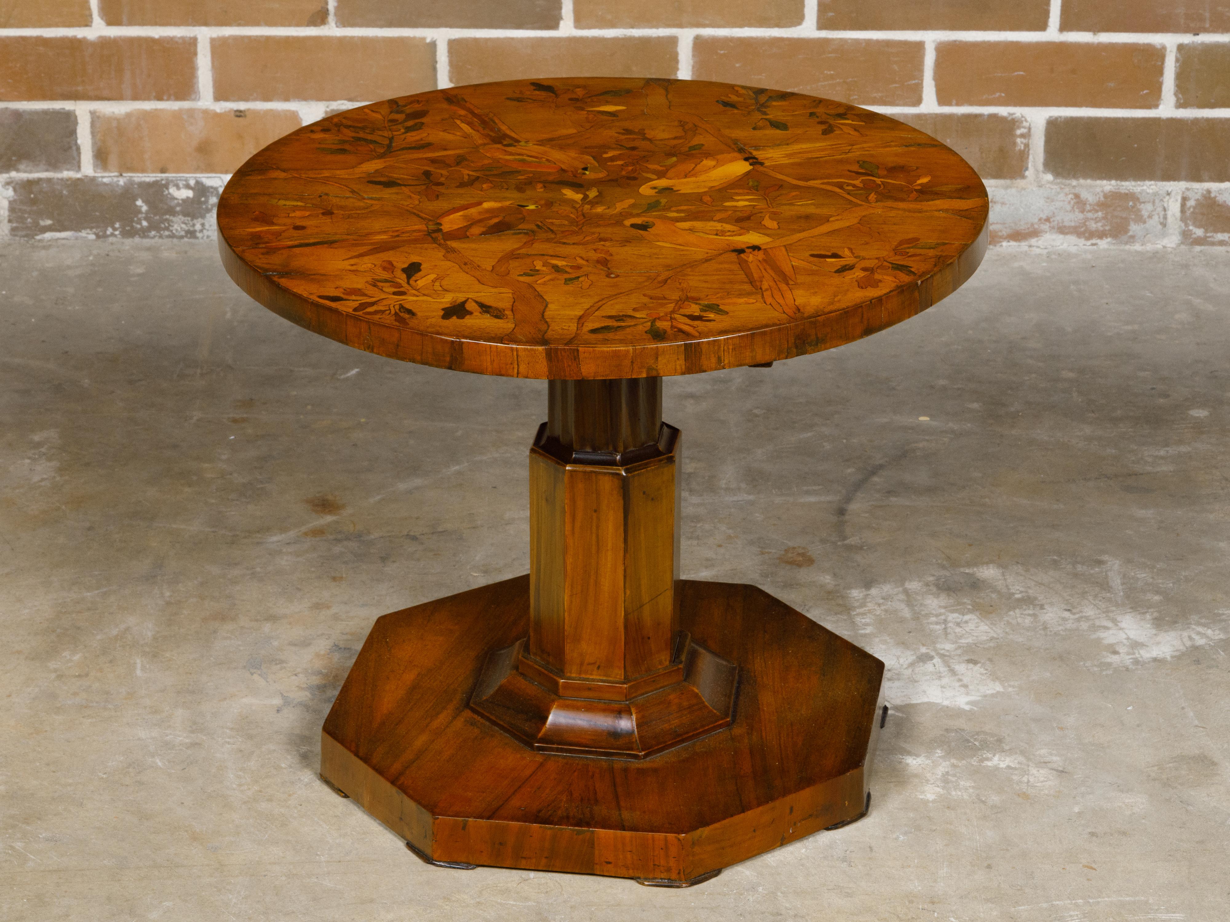 A Biedermeier period side table from the 19th century with parrots in branches marquetry and octagonal pedestal base. This Biedermeier period side table, hailing from the 19th century, is a splendid example of fine craftsmanship and artistic