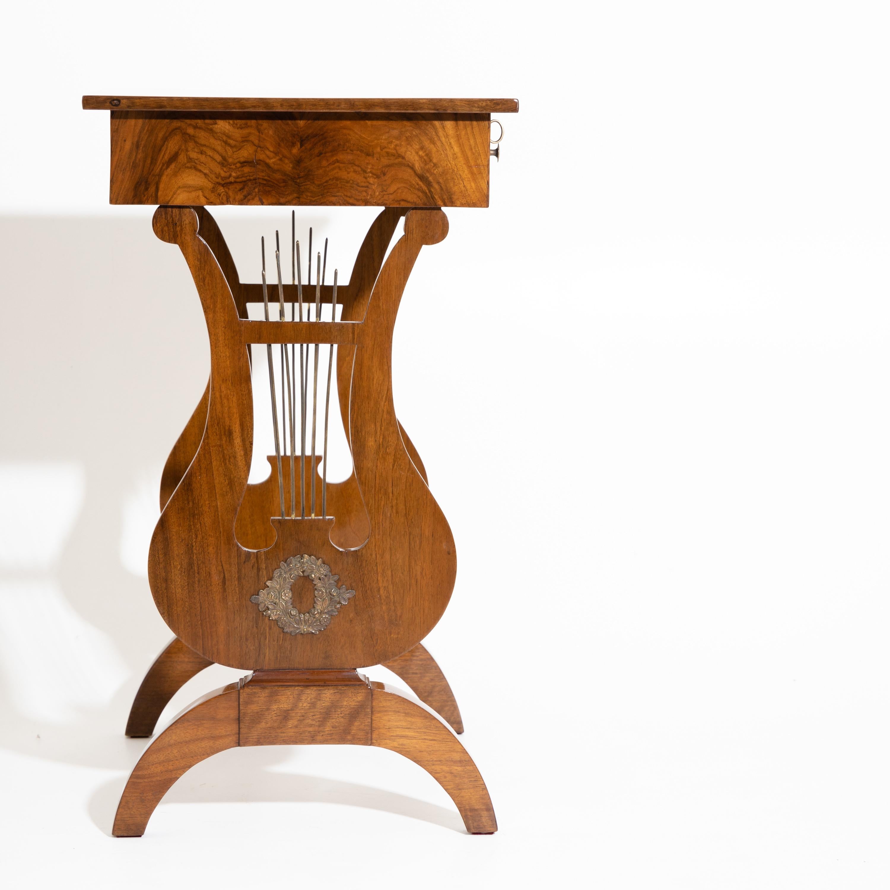Biedermeier side table on lyre legs with brass strings and decorations as well as one drawer with round brass knobs and practical interior division. The table is veneered in walnut and expertly hand polished.