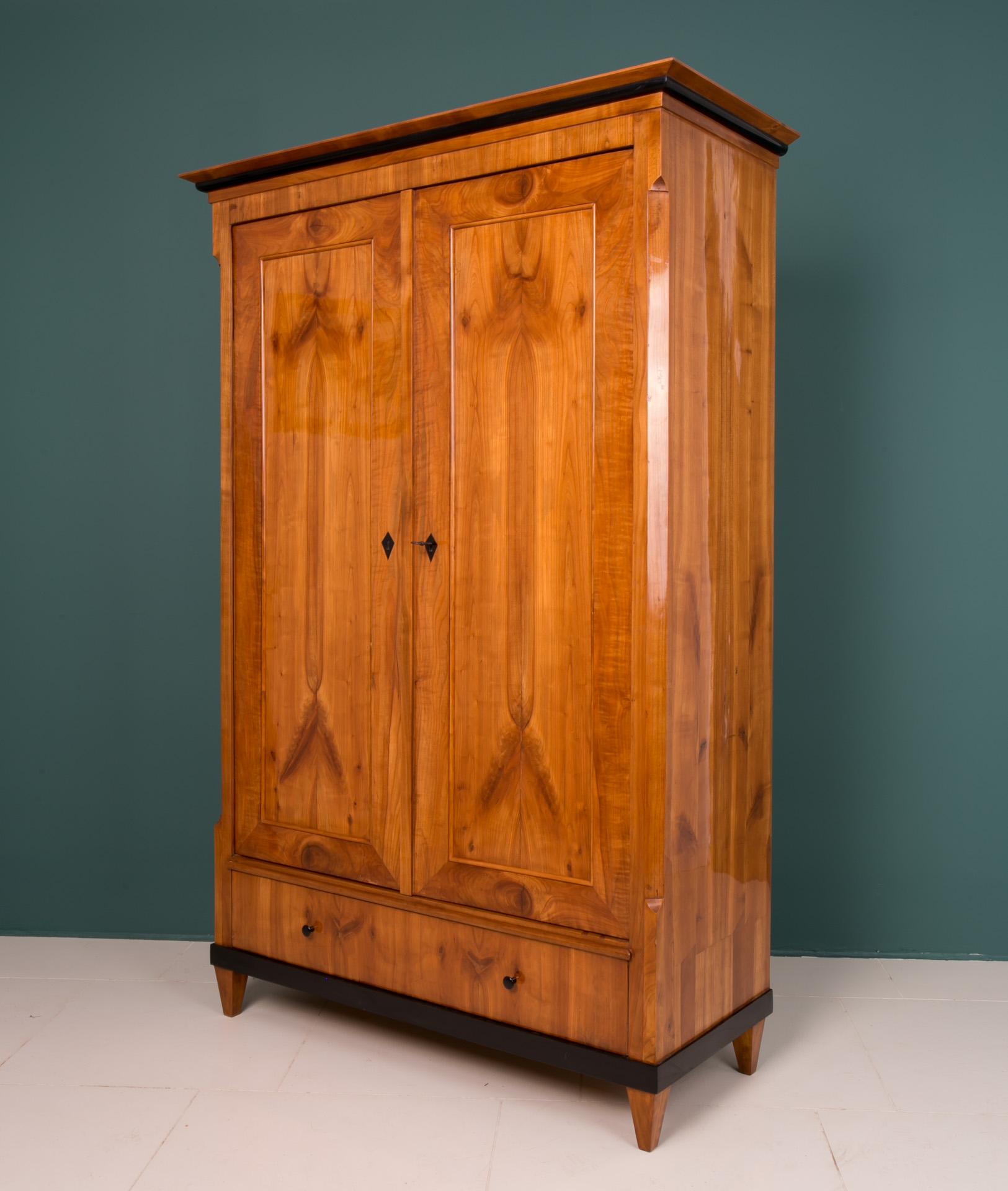 This Biedermeier wardrobe was made in Germany in first half of the 19th century. The piece is veneered with beautiful cherry wood veneer. It features one main storage section with a shelf and a hanging bar plus a practical drawer in the bottom.