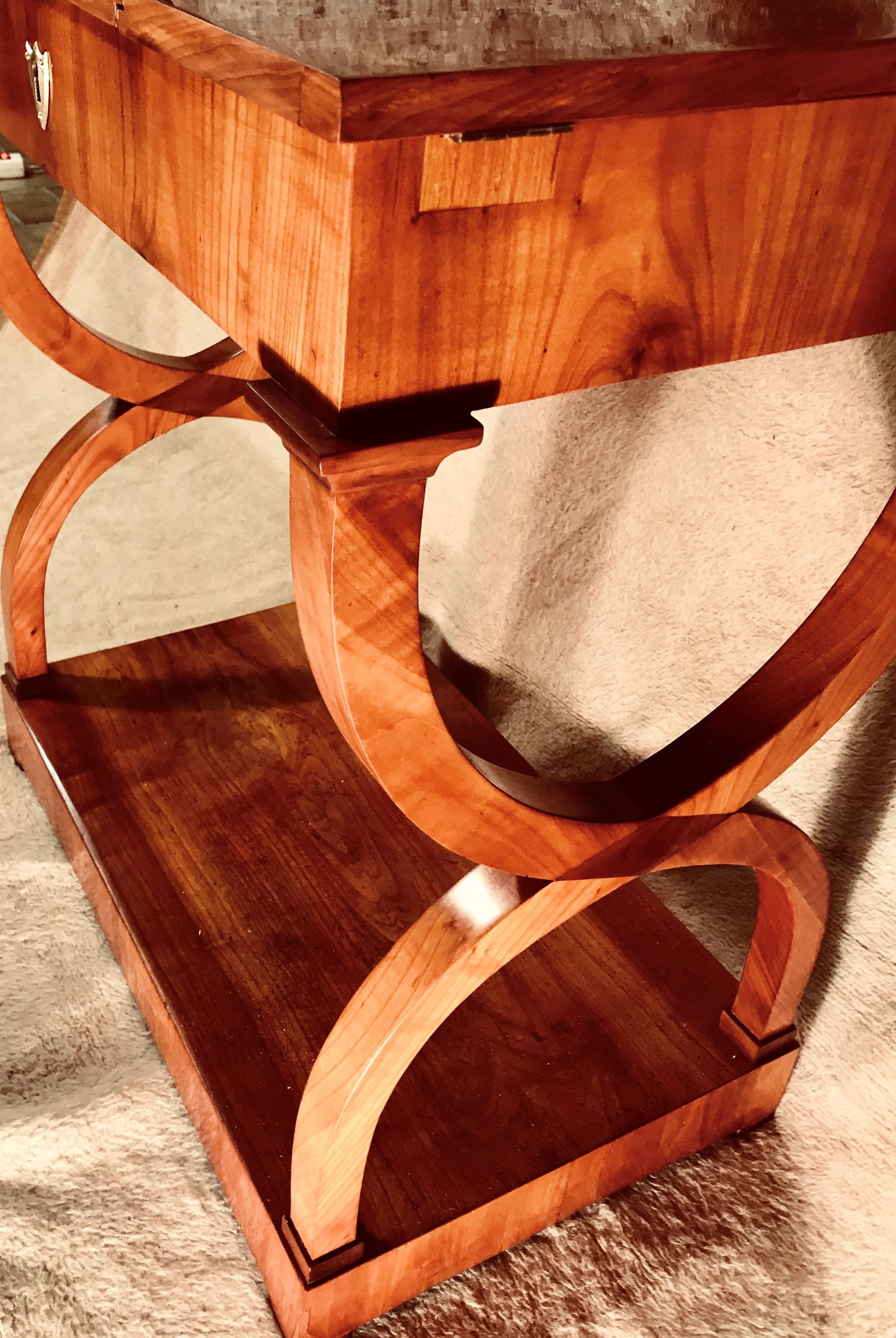Excepcional mesa de costura o de trabajo Biedermeier original, Múnich 1810-1820. La chapa de madera de cerezo embellece esta hermosa mesa. 
La parte superior está dividida en tres partes. La solapa central se abre primero y deja al descubierto 5