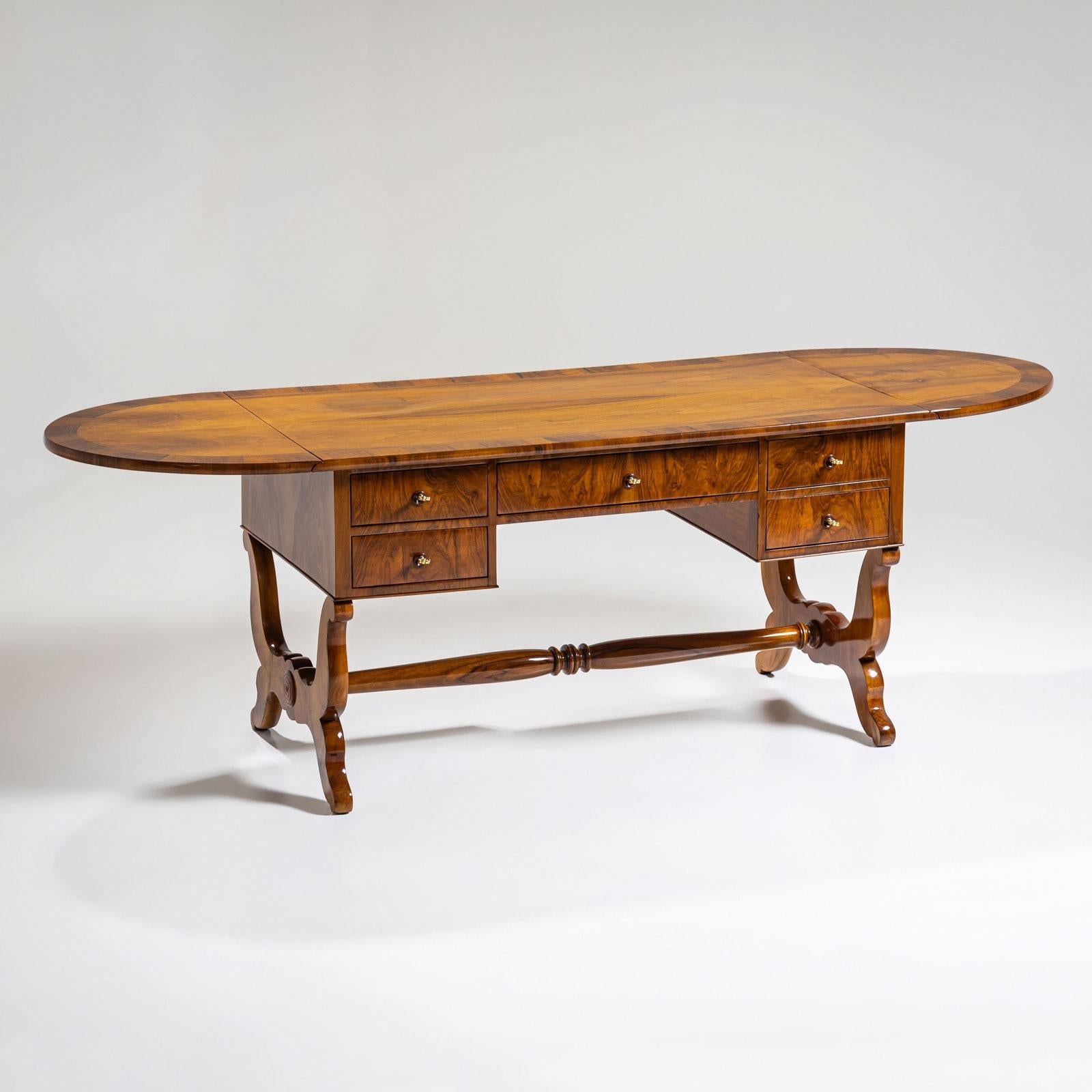 Biedermeier desk crafted from walnut, featuring gracefully curved legs and a baluster-shaped central stretcher. The desk offers ample storage with five drawers and an expandable writing surface that extends to a maximum length of 240 cm using the