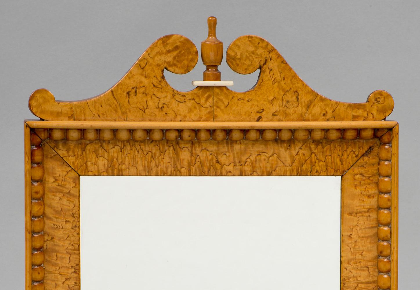 Biedermeir mirror in a burled maple frame, topped by a swan neck pediment with urn shaped finial on a bone base. The inside border has hand carved beading all around.