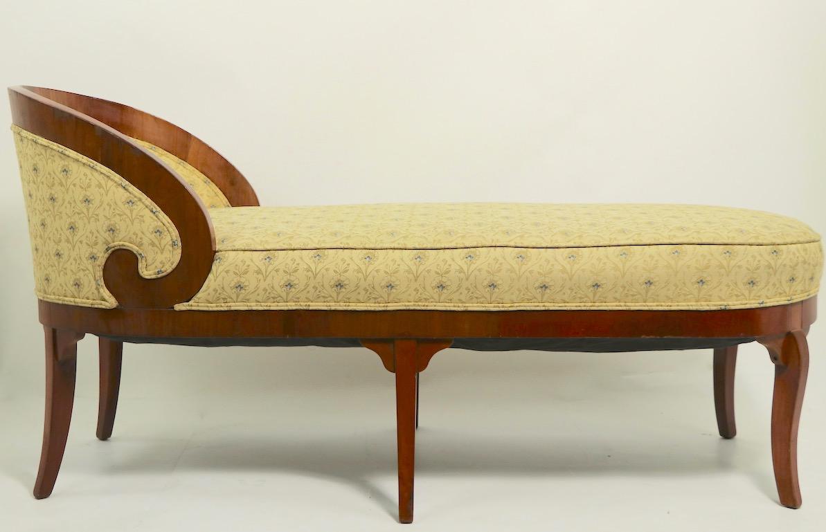 Chic and stylish Biedermeier chaise lounge of polished walnut and upholstered seat and back, fabric possibly William Morris. The chaise is in good condition, showing some loss to veneer trim, normal and consistent with age, please see images.