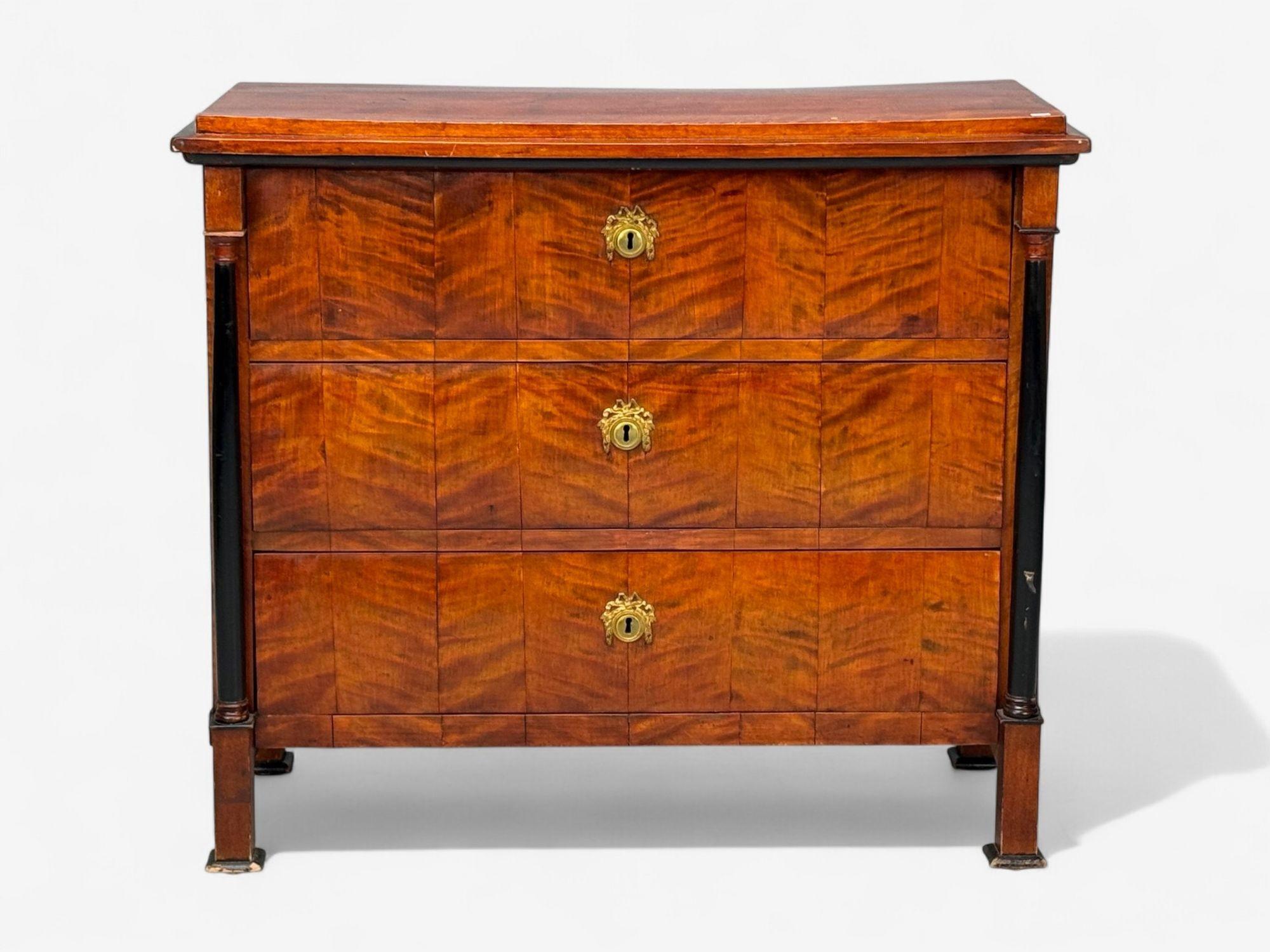 Biedermeier, impiallacciatura di ciliegio, ottone, legno ebanizzato, cassettone o comò, Germania, inizio XIX secolo.

Splendida cassettiera a tre cassetti con colonne in ebano che fiancheggiano una serie di cassetti con un raro piano rialzato e fori