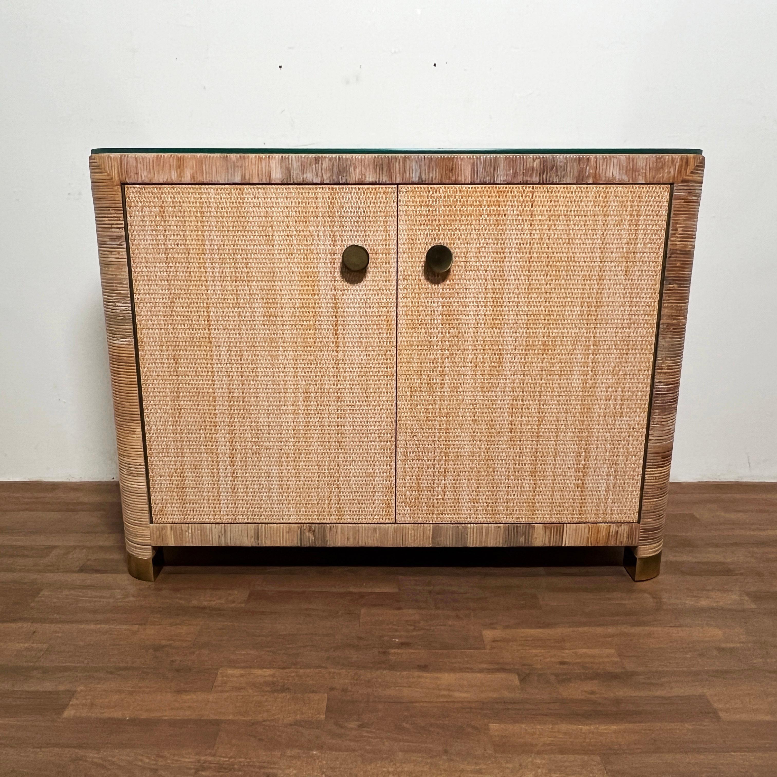 Two door cane and rattan wrapped cabinet by Bielecky Brothers of New York, circa 1980s. Brass clad feet, and brass handles, with bullnose front corners. Can be used with or without included glass top.