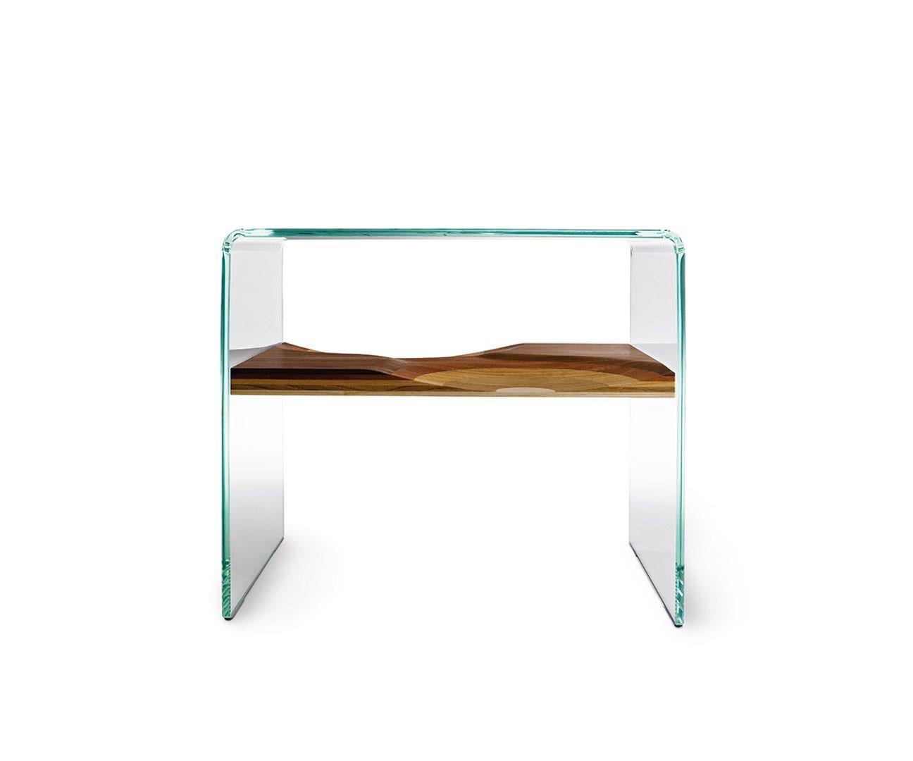 In Bifronte side table, a shelf made of five different solid woods is framed in a structure of extra clear glass, creating a “trompe l’oeil” effect of mid-air suspension.Curved extra-clear glass structure.Shelf made from plywood using five different