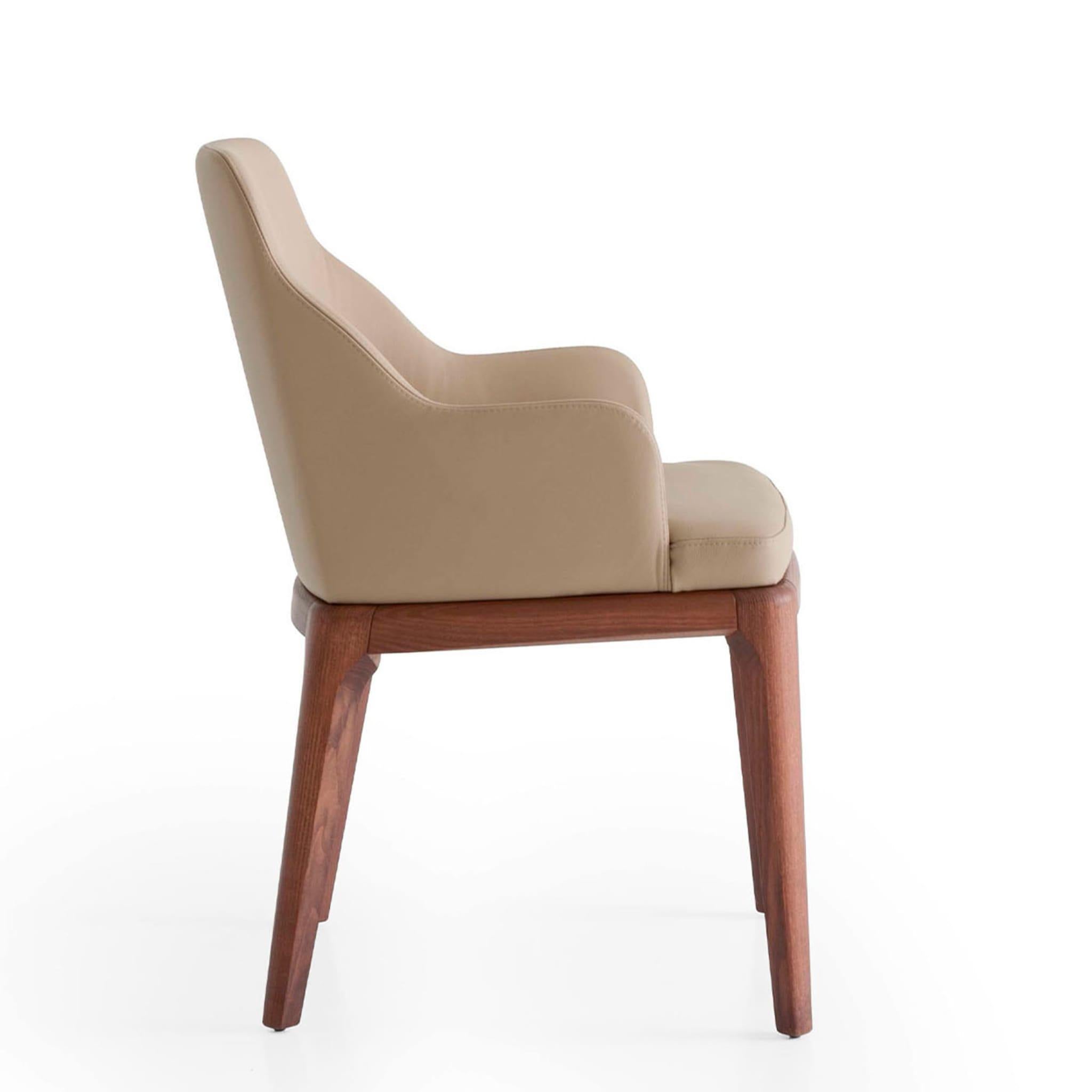 At once graceful and seductive, this armchair elegantly combines exclusive materials and warm neutrals. Sleek ash legs enriched with walnut stain sustain the seating unit, its enveloping wooden shell marked by sinuously sloped sides incorporating