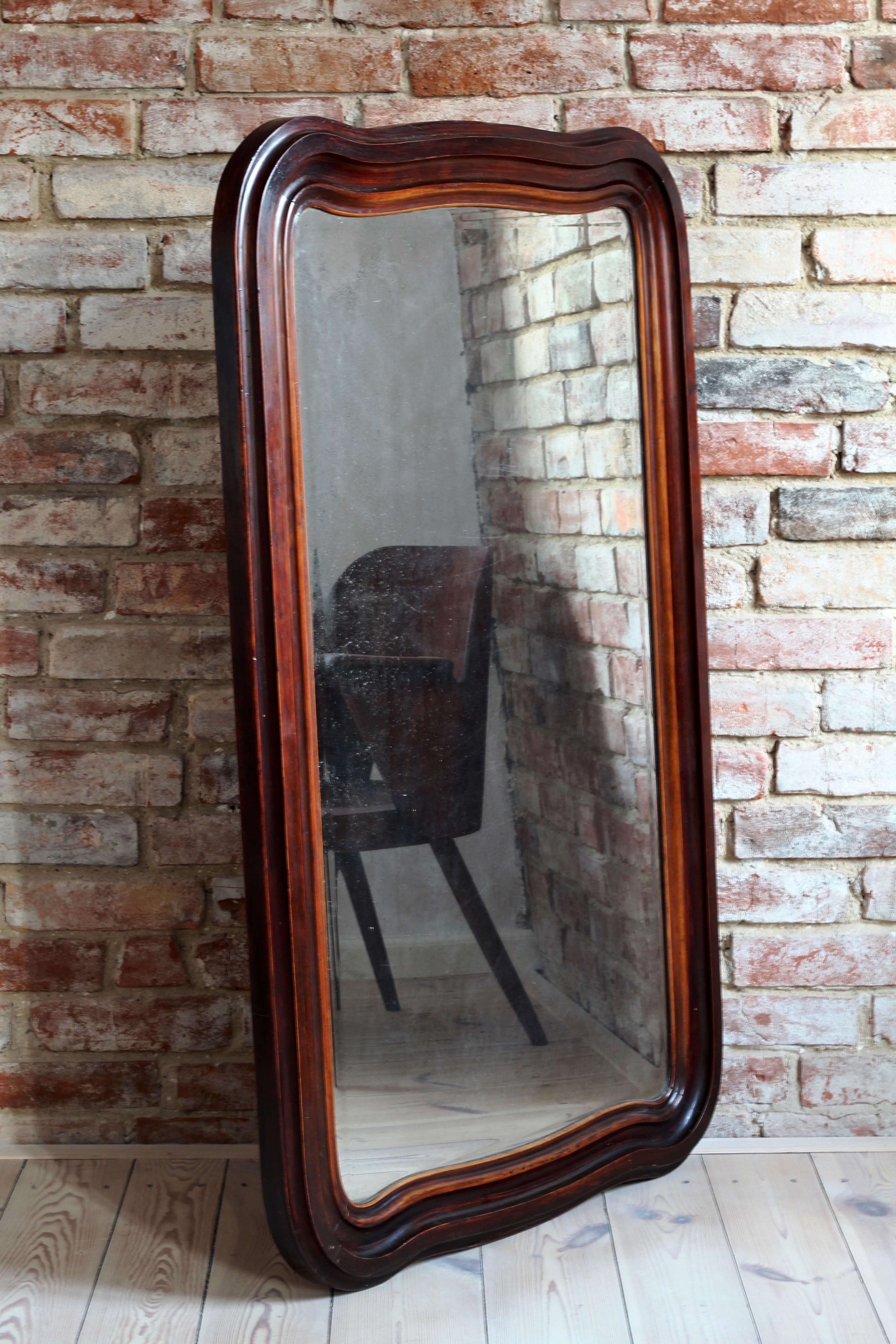 This big antique mirror is a perfect example of how time and patina can decorate an everyday life object. The surface of the mirror is still clear enough to reflect the image but got old in a unique unrepeatable way. The solid wooden frame features