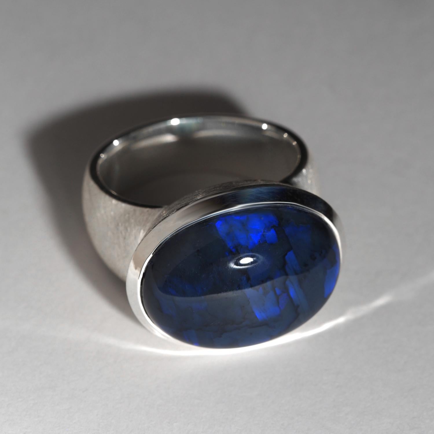 This beautiful and bold ring features a natural Australian black opal with an intriguing pattern reminiscent of lightning in a dark sky. The opal displays a mesmerizing inky navy blue hue with a stunning play of color, making it an eye-catching