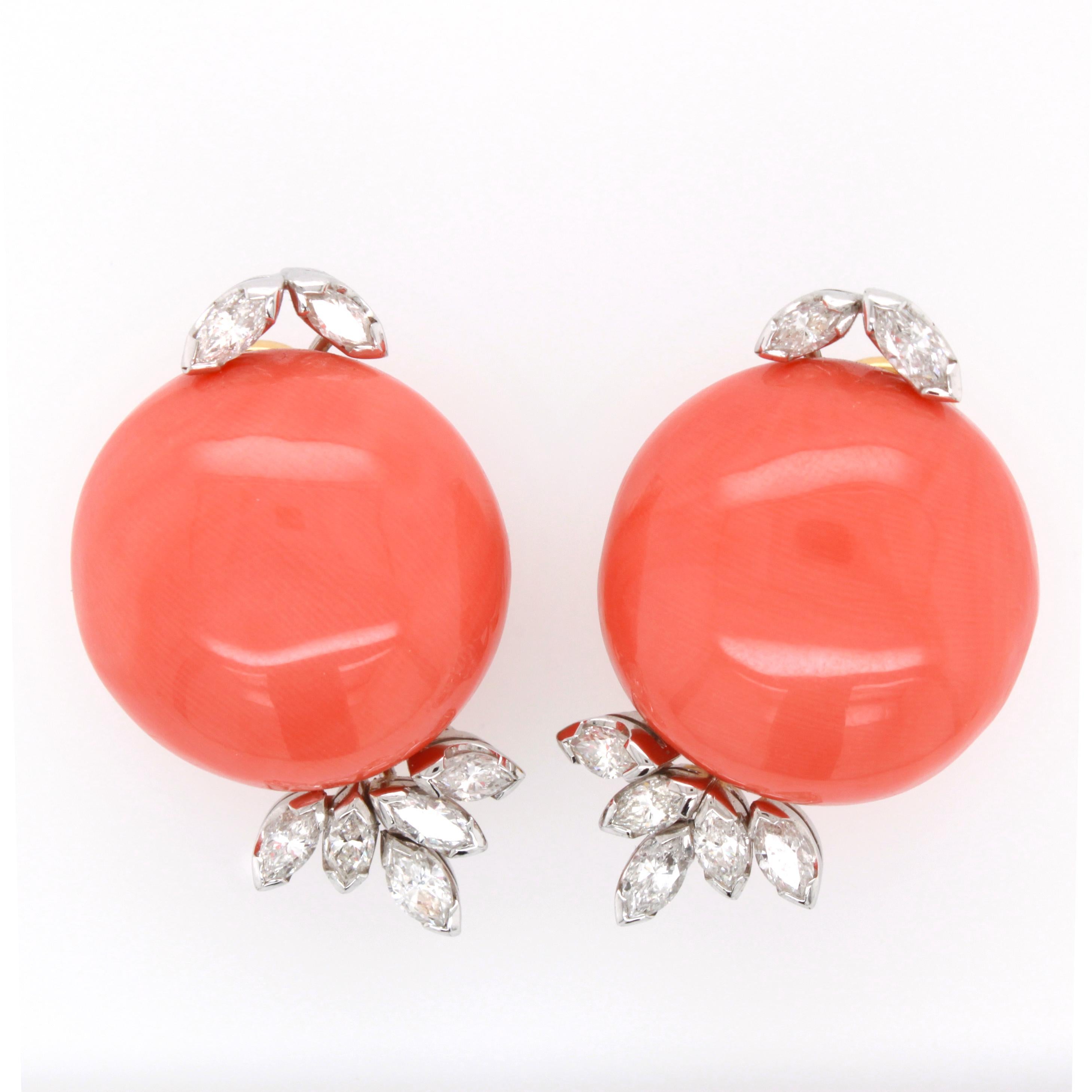 A pair of earclips, each with a big coral cabochon and marquise cut diamonds. The corals have a diameter of 21mm and the total diamond weight is approximately 1.5 carats. The earrings have the 18k yellow gold stamp and Italian marks.