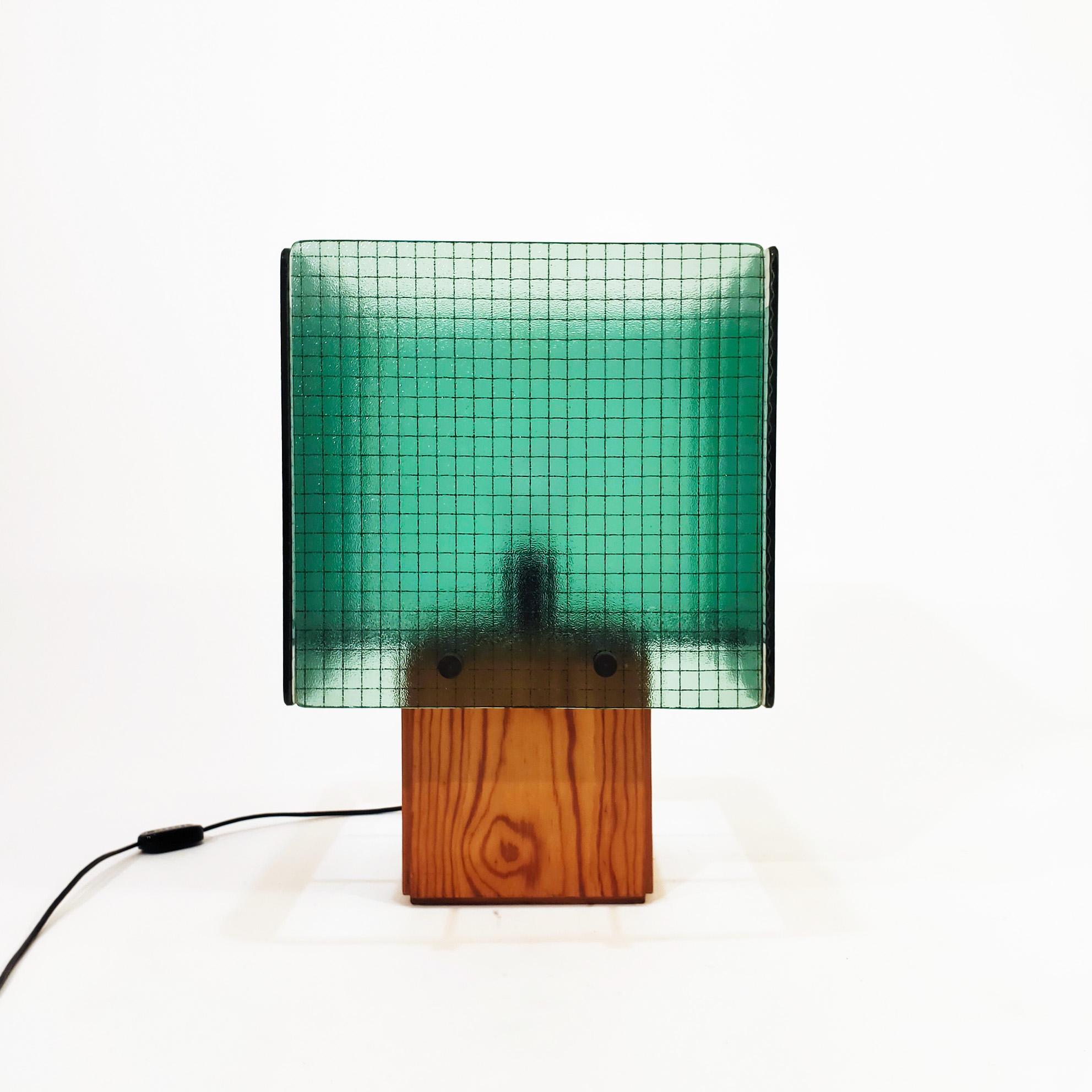 Large cubist table lamp with a certain Memphis style from the late 70s, made in Spain. Composed of a prismatic base of pine wood and an upper screen formed by four square planes of green reinforced safety glass, through which the light is projected