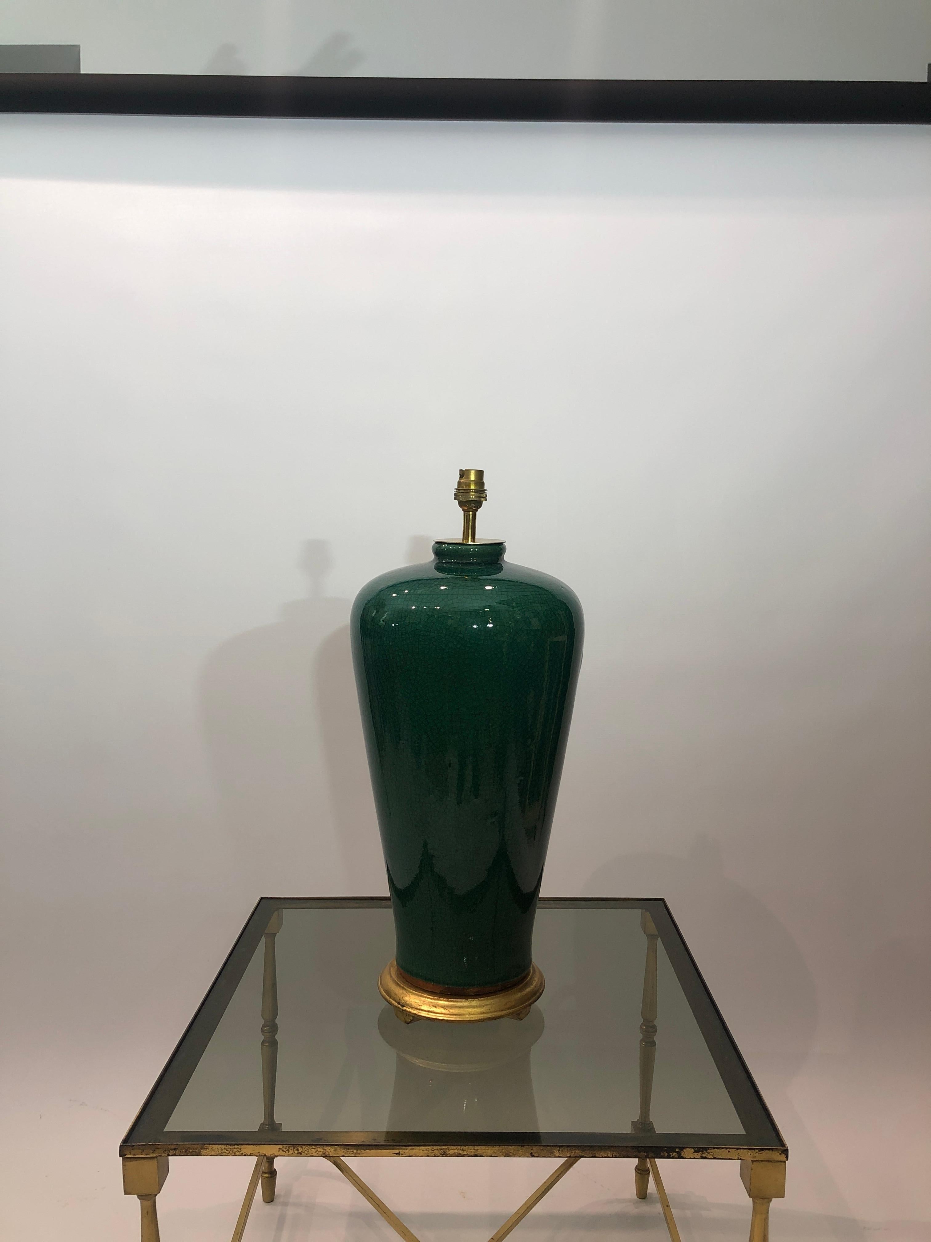 Eine elegante hohe smaragdgrüne Keramik mit Rissglasur und Messingbeschlägen, die auf einem runden, goldfarbenen Sockel steht. Ein klassisches Design, das sich durch seine Präsenz auszeichnet.

Die Lampe würde in den meisten Interieurs hervorragend