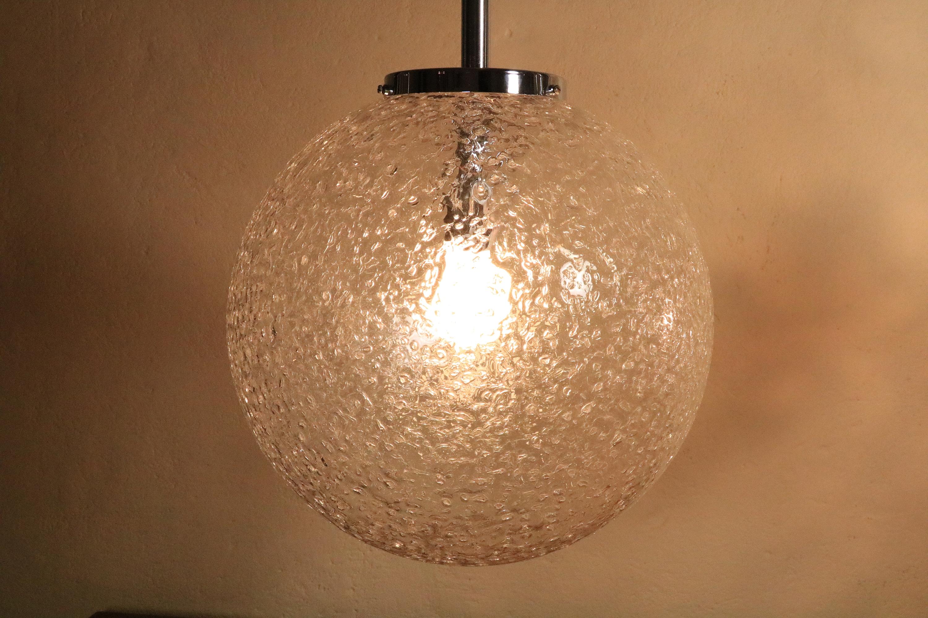 A total of three large ball lamps made of textured thick bubble glass.
Beautiful chrome finish held by three screws on the neck of the ball.
 
Manufacturer could be DORIA.
 
Diameter: 35 cm / 13.77 inch
White textile cable with steel cable