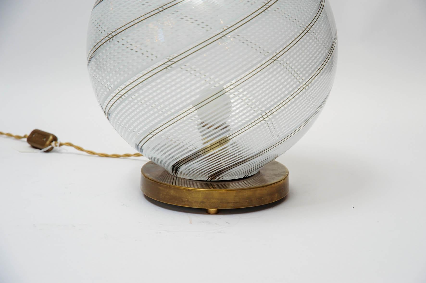 Table lamp made of a patinated brass circular foot with original stamp, topped with a large Murano glass globes with the typical Venini swirl stripes.