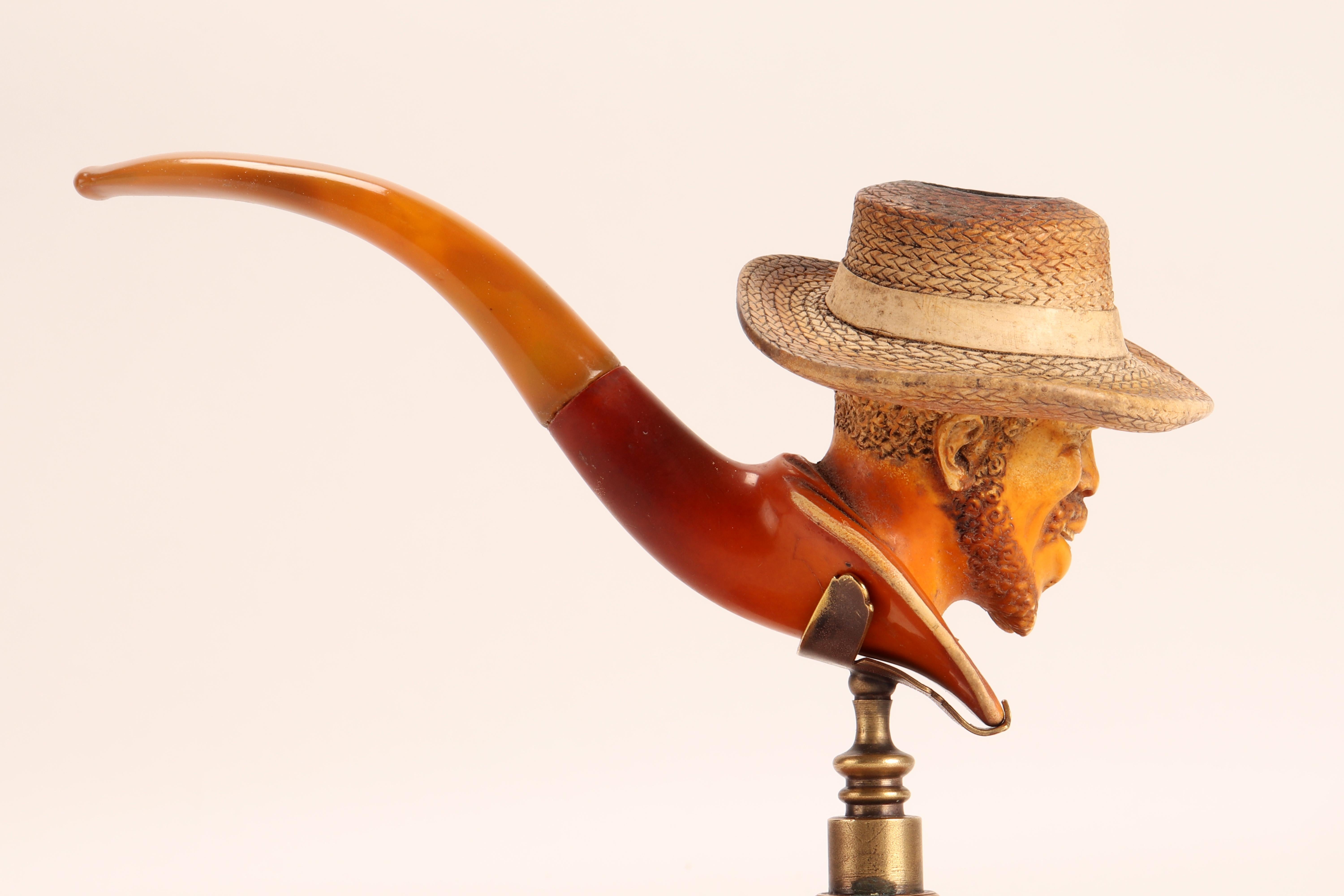Carved meershaum pipe, with amber mouthpiece. In the large bowl of the pipe, the head of an African American smiling man is depicted, with a straw hat. Original case. Vienna, Austria circa 1880. (The stand is for photographic use only, not for sale).