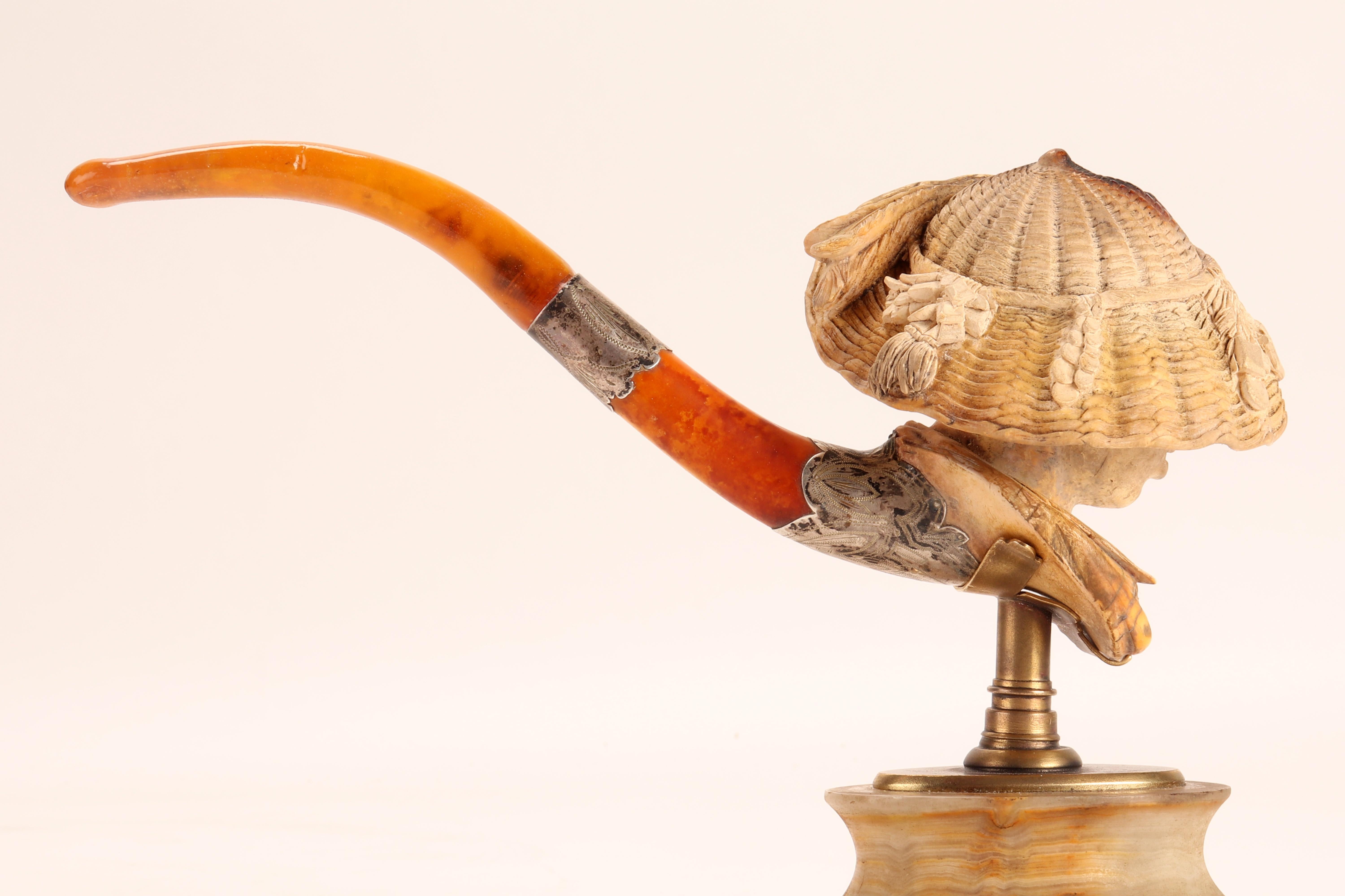 Carved meershaum pipe, with amber mouthpiece and nielloed silver band. In the large bowl of the pipe, the head of an African American woman with hearing is depicted, with a wide straw hat with bows. Original case. Vienna, Austria circa 1880. (The