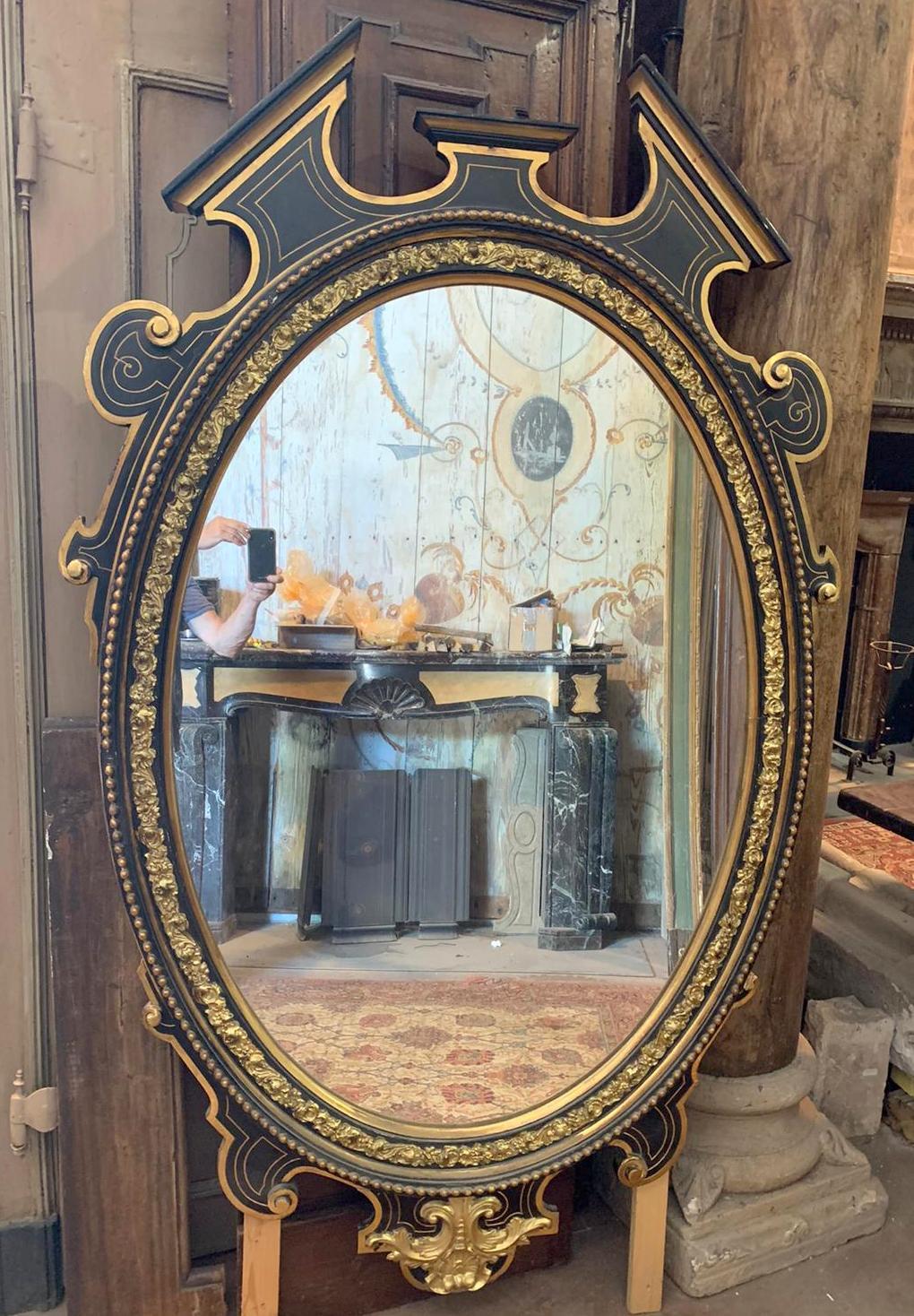 Vintage oval mirror, in black and gold lacquered wood, with carved frills and particular shape, built in the late 19th century in Italy.
Originally it was placed above a fireplace in a room with high ceilings, but currently it can be installed in