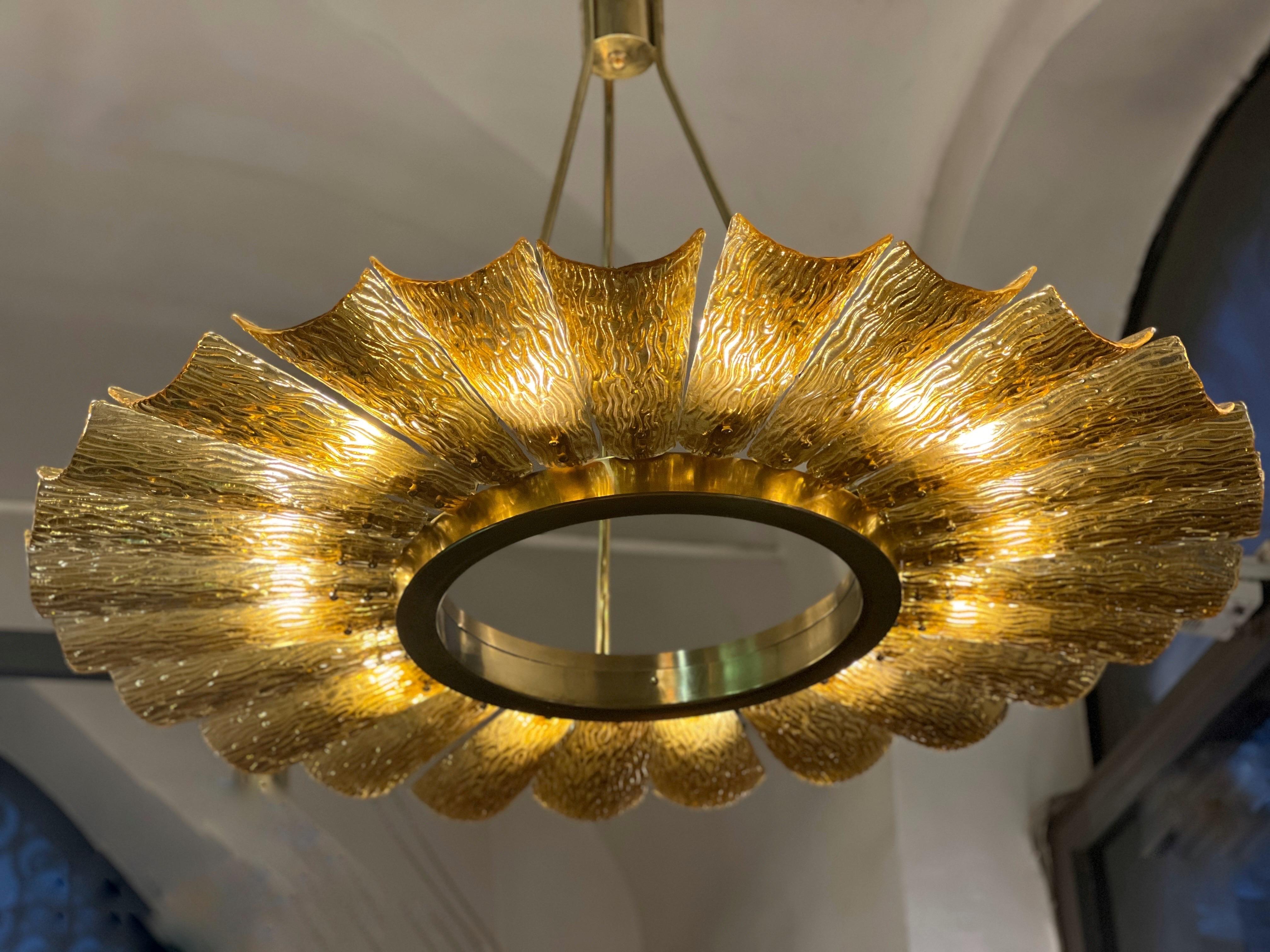 Lampadario rotondo d'epoca in vetro ambrato e ottone di Murano.
Il lampadario è realizzato in vetro di Murano color ambra con macchie d'oro soffiate all'interno. Le foglie soffiate e intrecciate a mano si susseguono intorno a un cerchio di