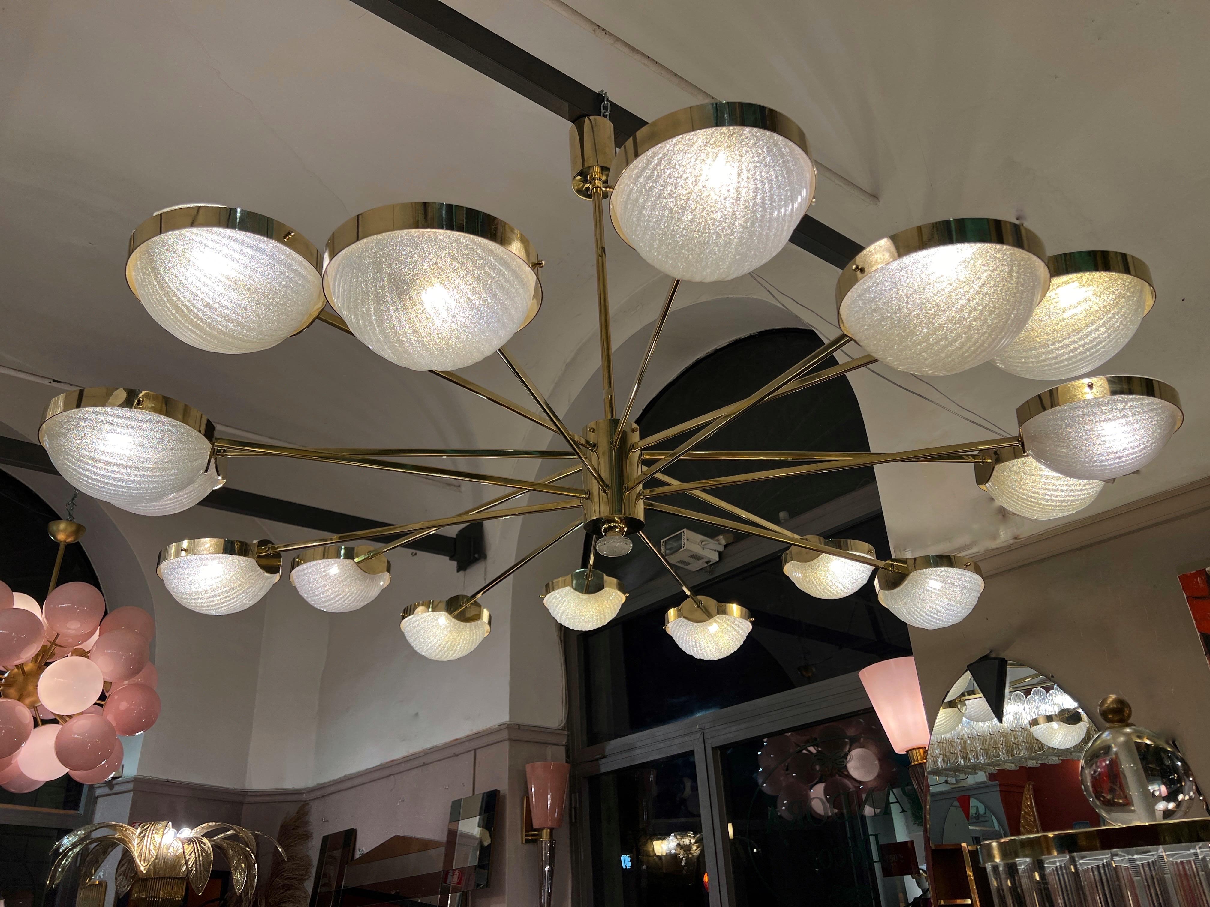 Grande lampadario rotondo in vetro trasparente di Murano e bracci sfalsati in ottone.
Il bicchiere vintage è  di Vistosi (Murano) ha un effetto smerigliato e a coste.
Il lampadario è dotato di 16 bracci in ottone sfalsati e di altrettanti bracci in