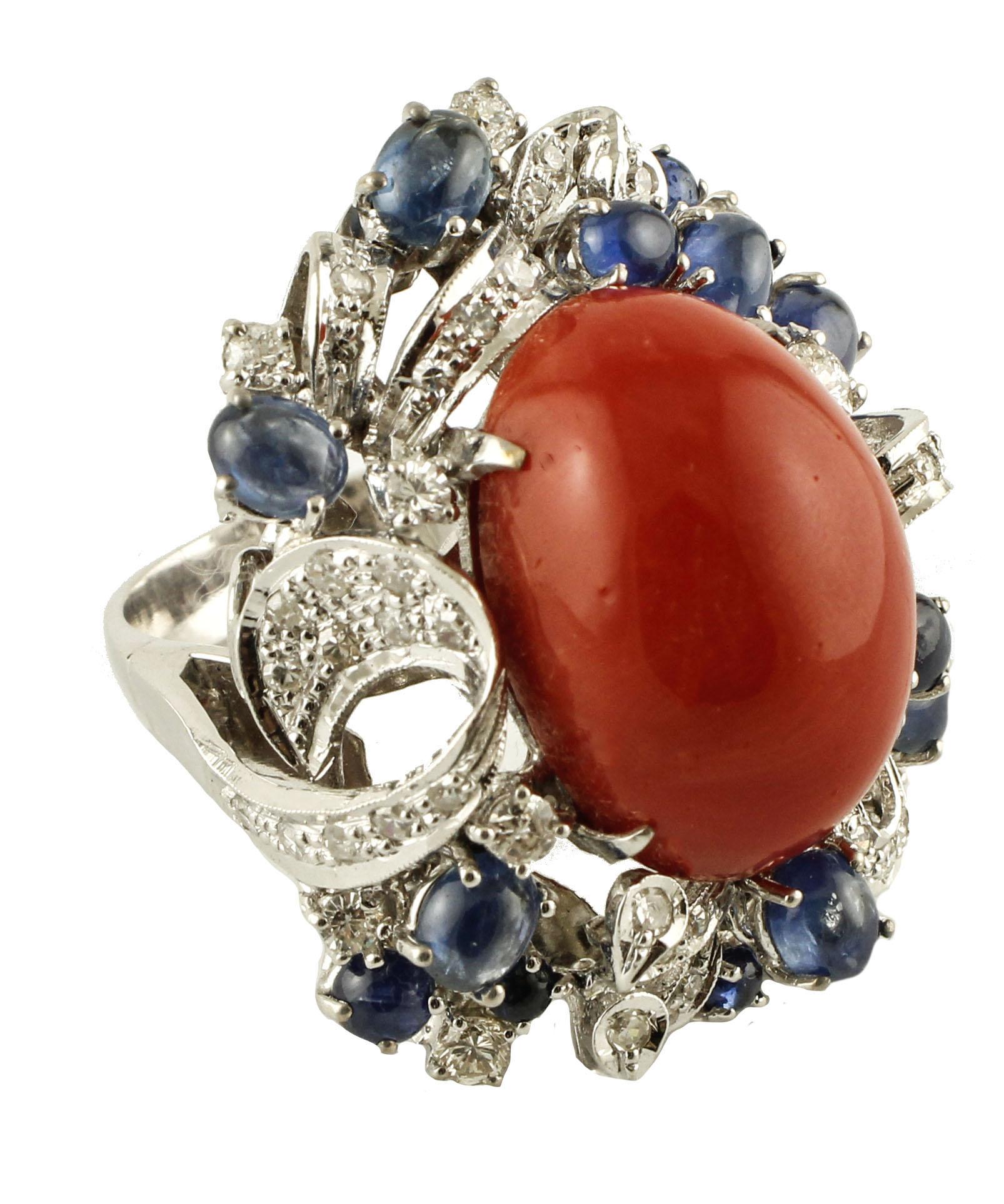 Wonderful Cocktail ring in 14k white gold structure. The ring is mounted with a big rubrum coral in the centre surrounded by white diamonds and blue sapphires adornments.  
This ring is totally handmade by Italian master goldsmiths
Diamonds 1.99