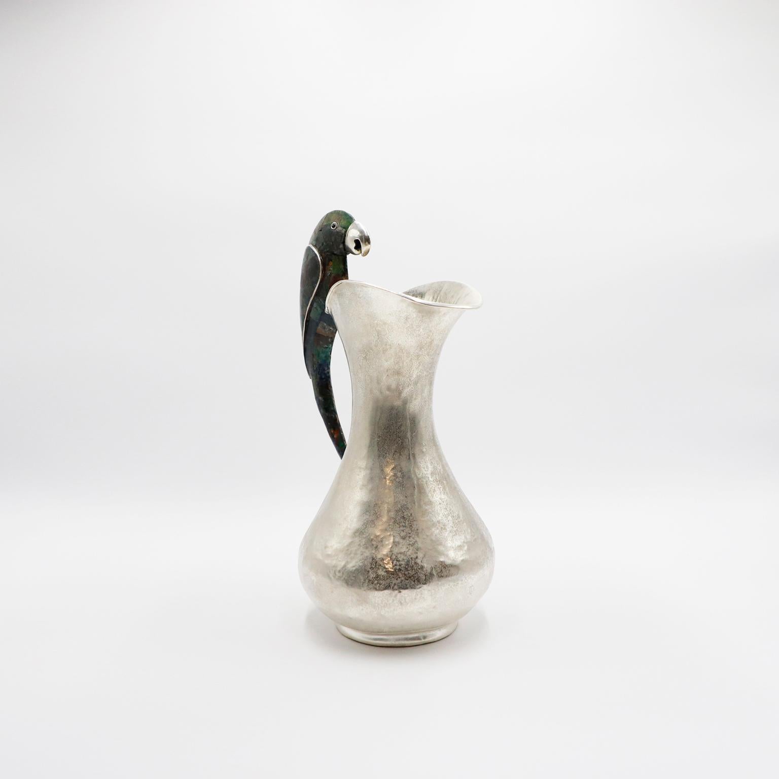 Alrededor de 1960. Te ofrecemos esta jarra mexicana de gran tamaño chapada en plata y malaquita que luce un asombroso asa con motivo de loro, de Los Castillo Taxco México. Se trata de un exquisito y monumental cántaro con el sello de Los Castillo y
