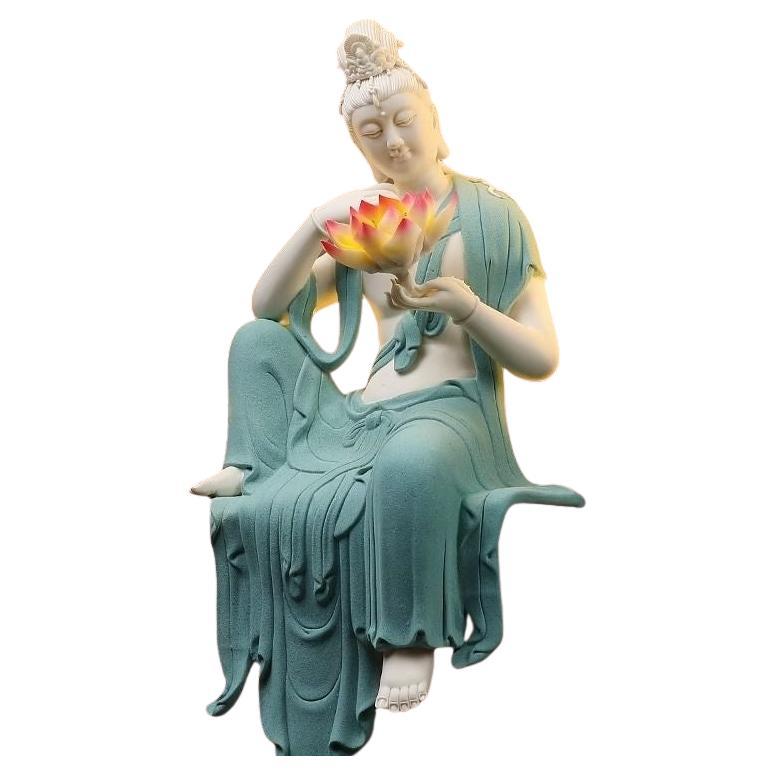 The big white porcelain statue of a sitting Buddha dressed in a blue robe and holding a lotus flower is a striking piece that combines artistry with profound spiritual symbolism.

White porcelain, particularly from renowned Chinese kilns such as